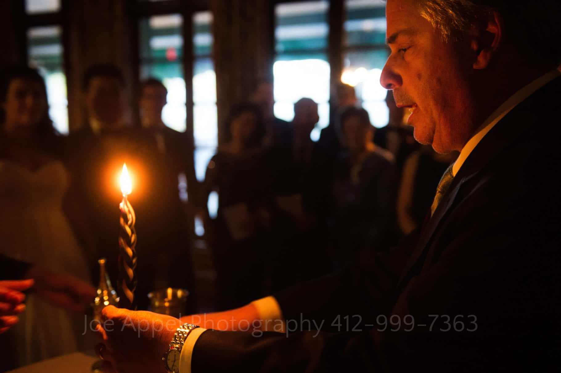 A rabbi chants a prayer as he holds a lit candle during a ketubah signing ceremony