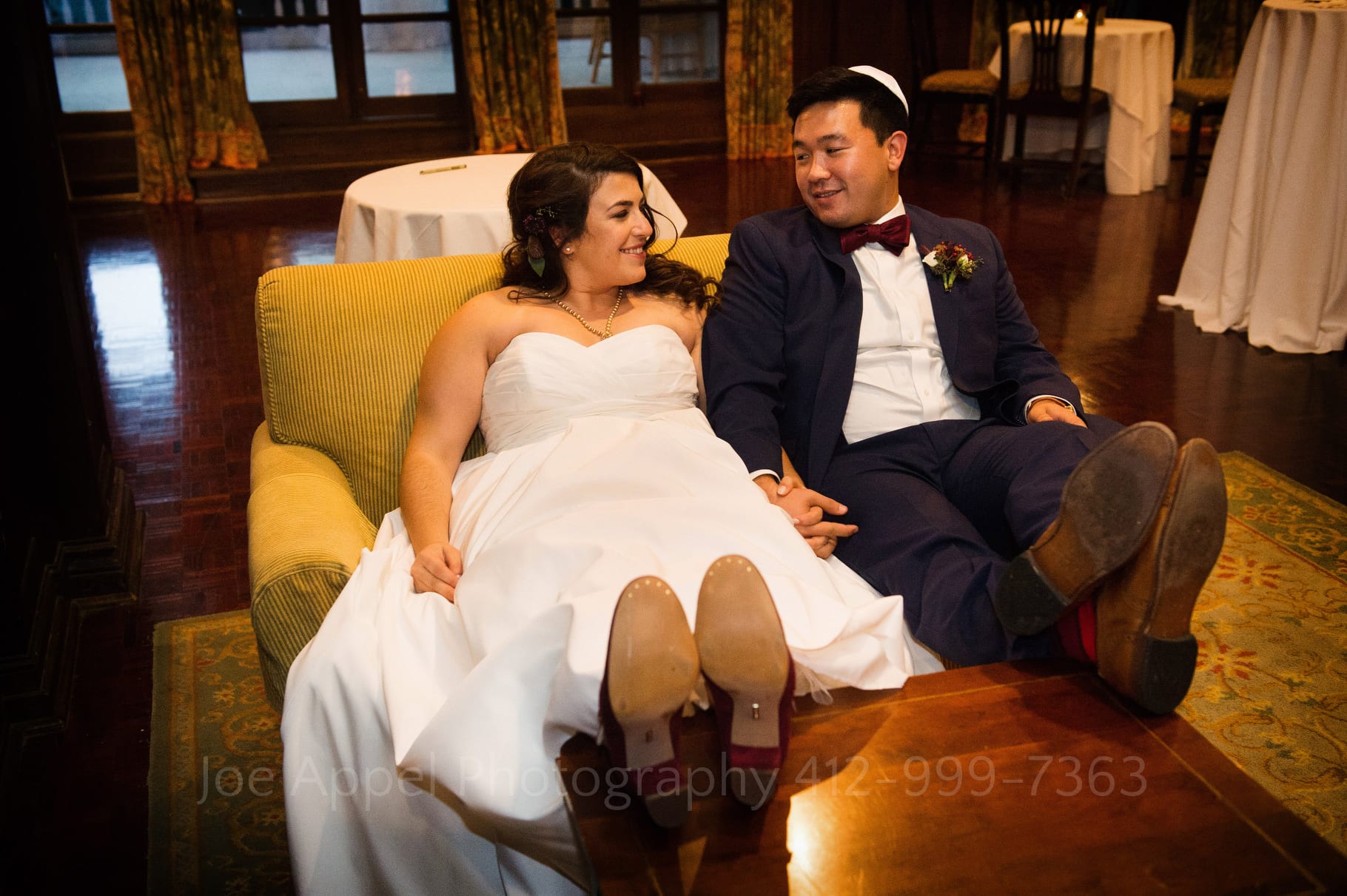 Bride and groom relax as they sit next to one another with their feet up on a table.