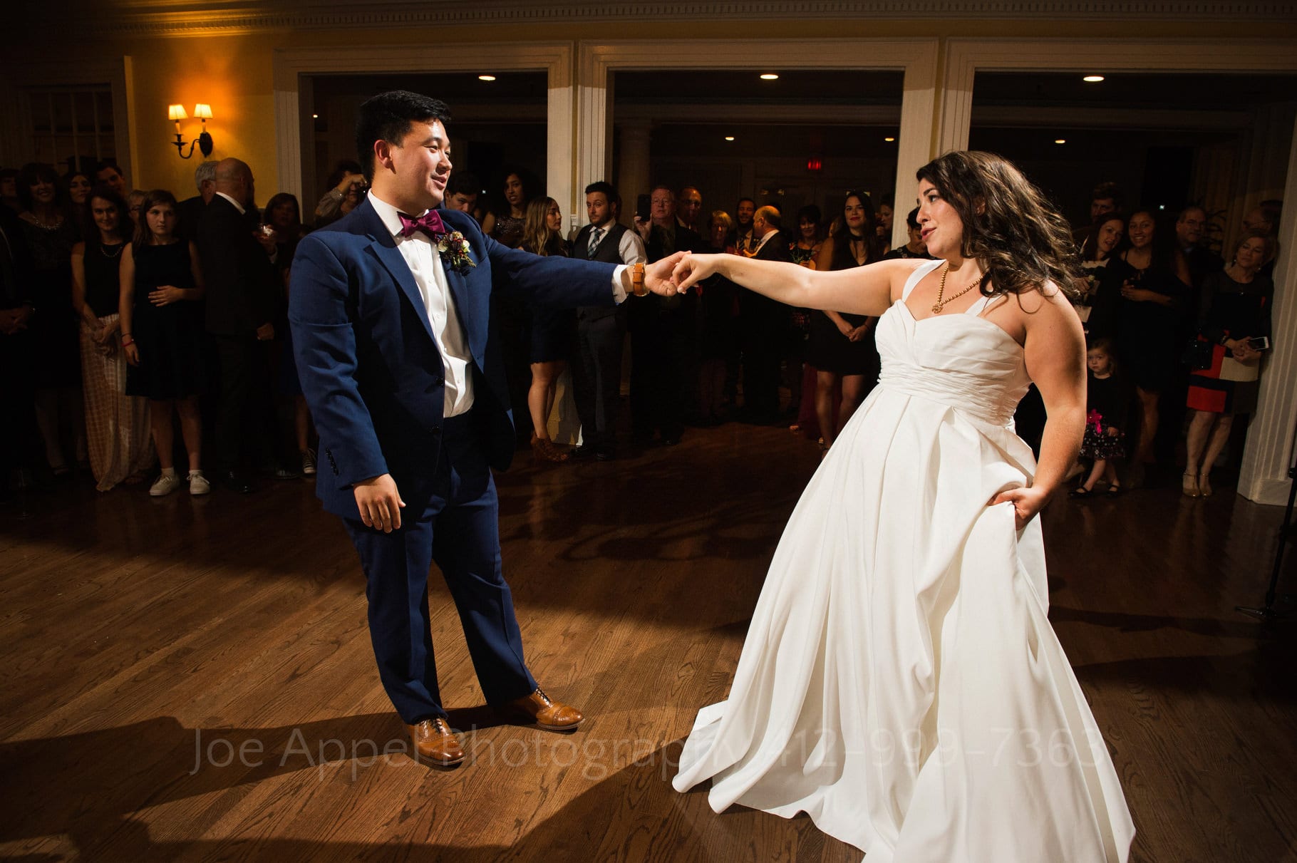 Bride and groom stretch out their arms as they hold hands while dancing