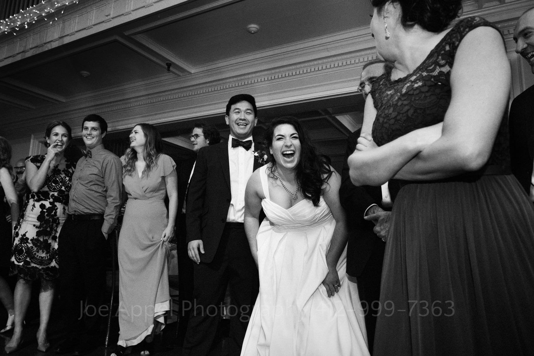 Bride bends at the waist as she laughs while watching her guests dance.