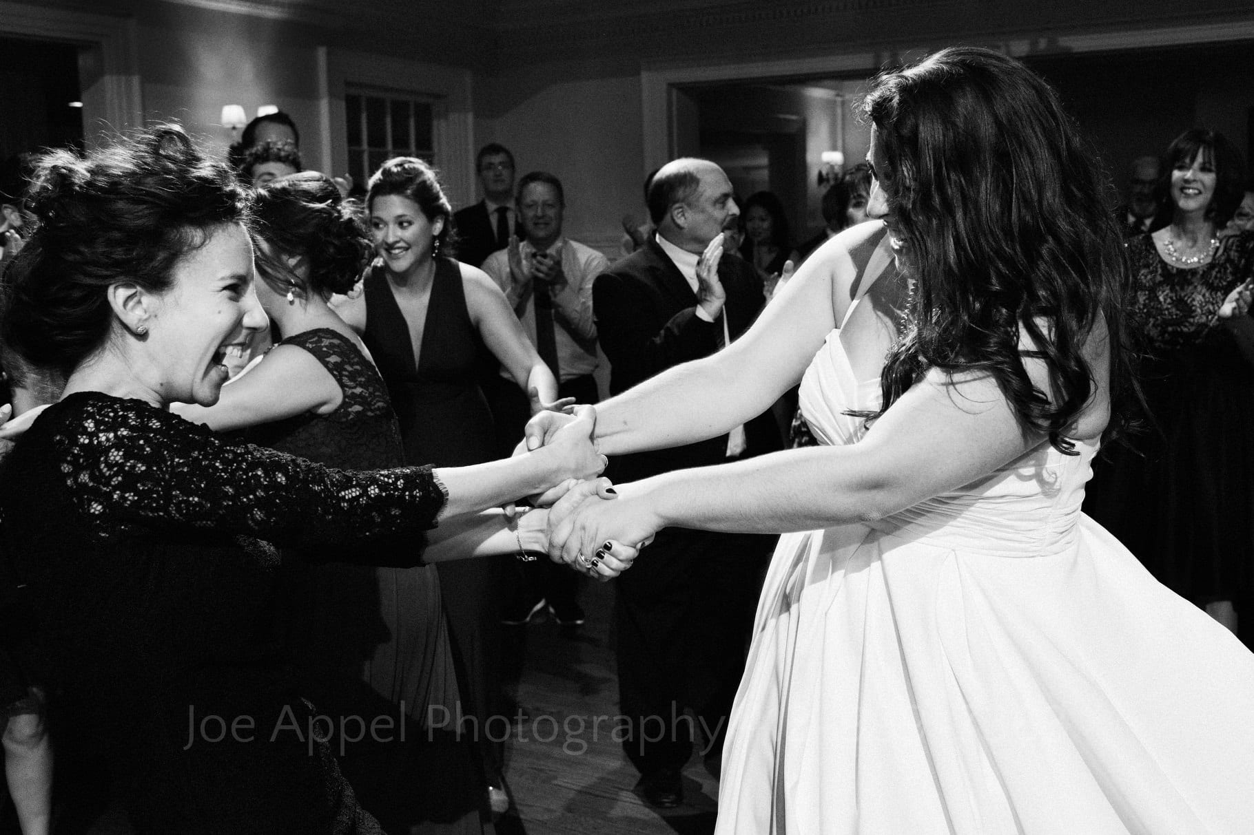 Bride holds hands with another woman as they spin around in a circle while dancing