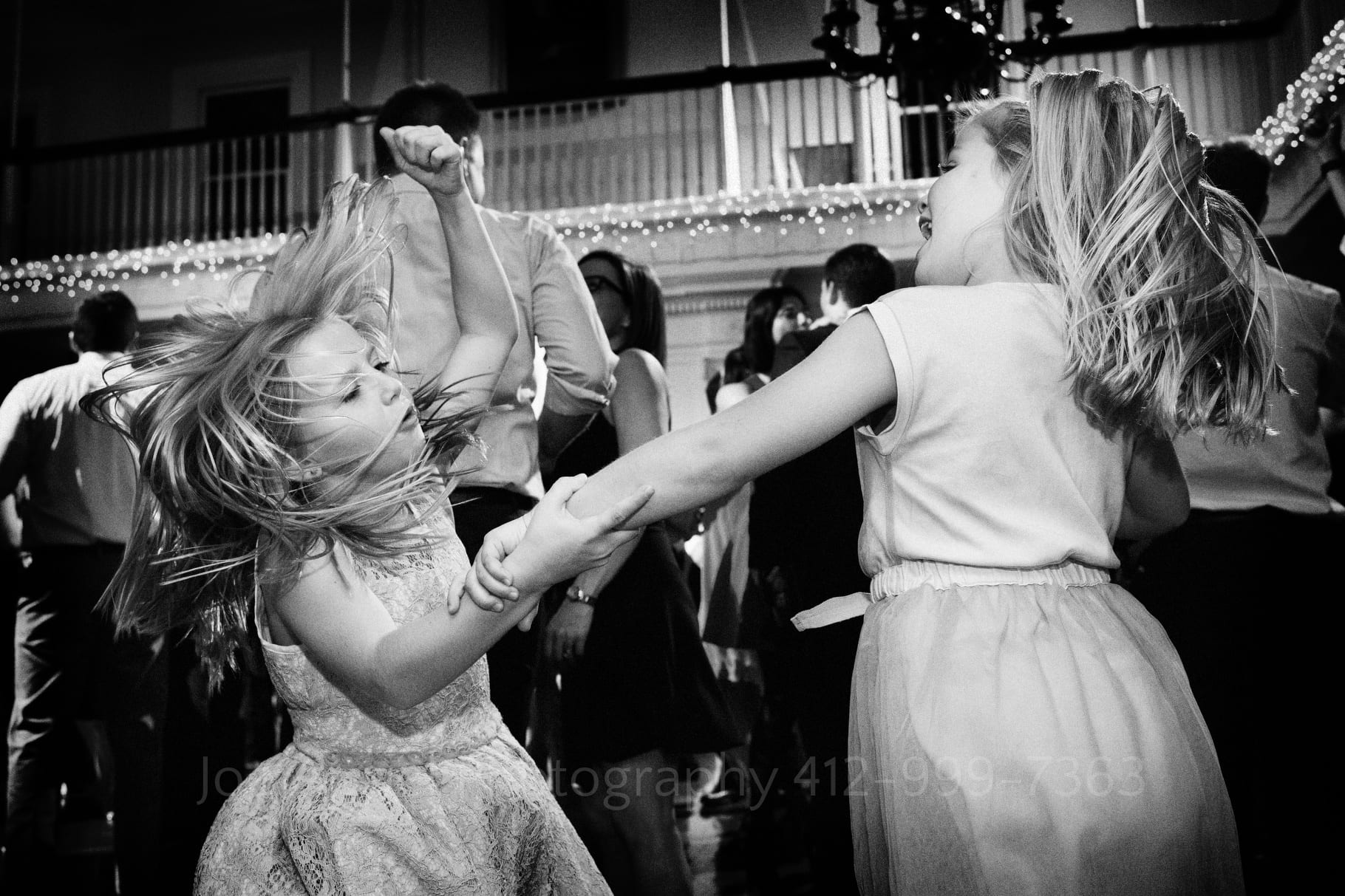 A little blonde girl raises her fist in the air as her hair flies up while dancing with another young girl at a wedding reception.
