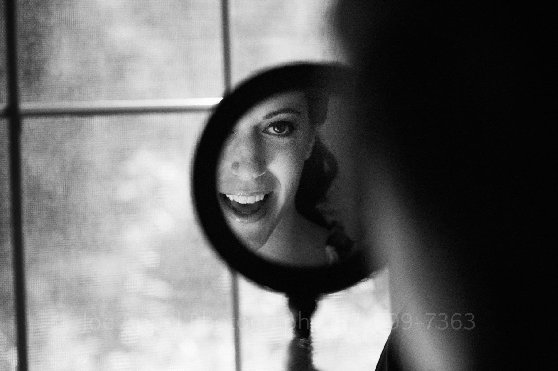 A woman grins as she looks at her reflection in a round mirror in front of a window