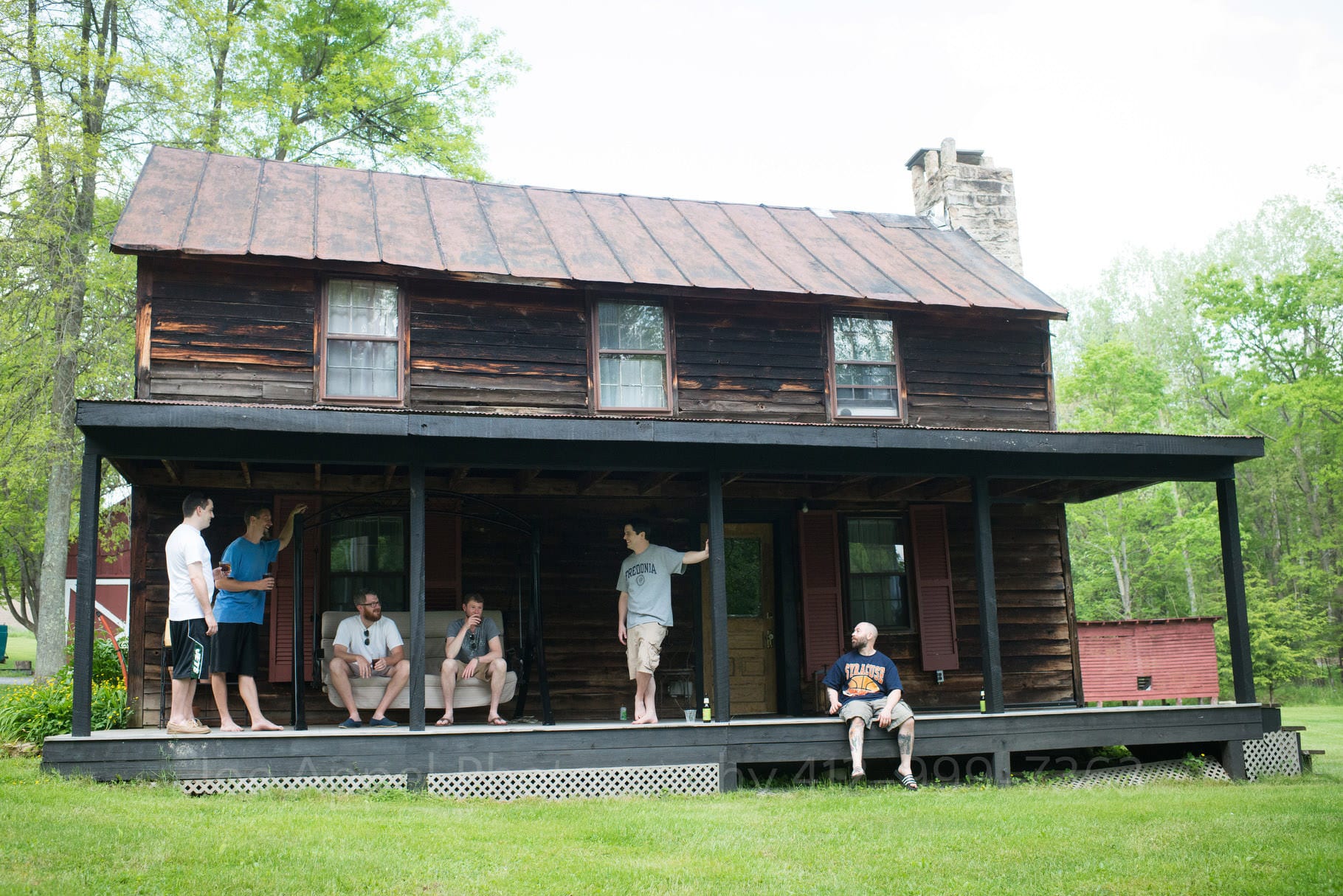 five men in a bridal party relax on the front porch of a rustic wooden cabin during their Chanteclaire Farm Wedding.