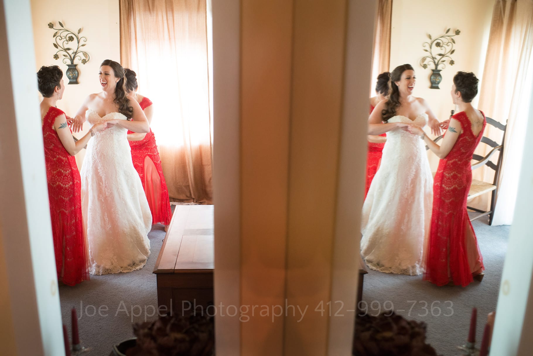A double view of a bride being helped into her wedding dress caused by a reflection in a bathroom mirror