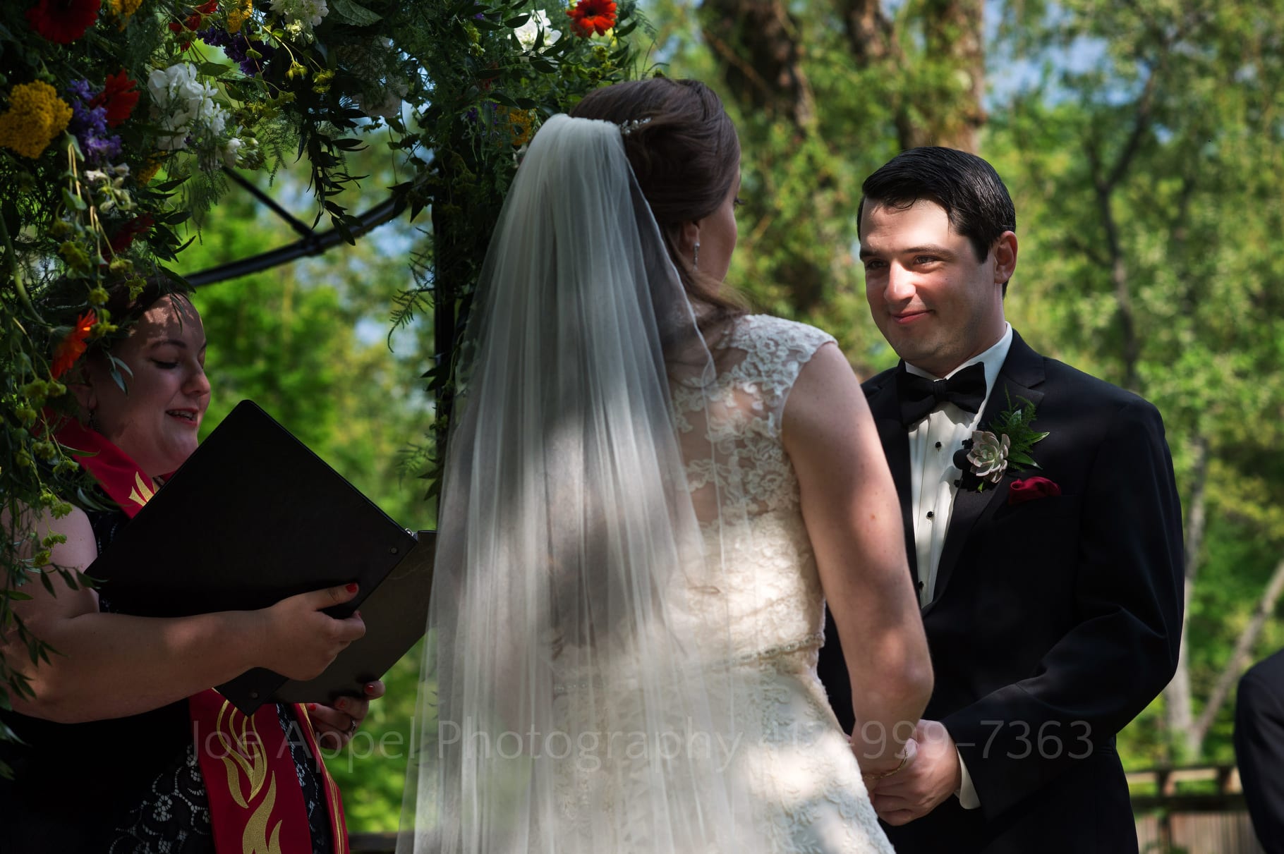 dappled sun illuminates just the face of a groom as he says his vows while facing his bride during their Chanteclaire Farm Wedding.