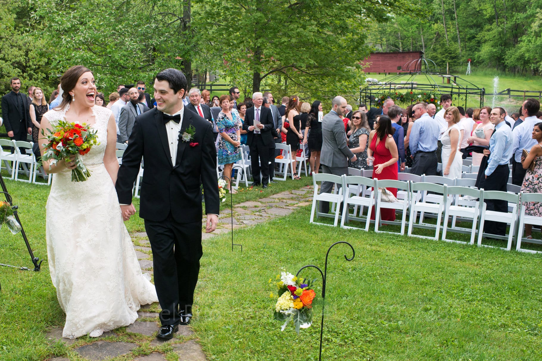 bride and groom exit their outdoor wedding ceremony hand in hand along a stone path during their Chanteclaire Farm Wedding.