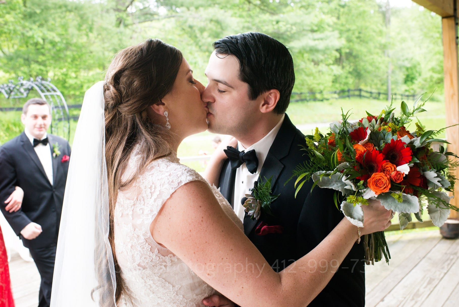 bride and groom embrace and kiss immediately after their wedding. the bride is holding a red and orange bouquet during their Chanteclaire Farm Wedding.