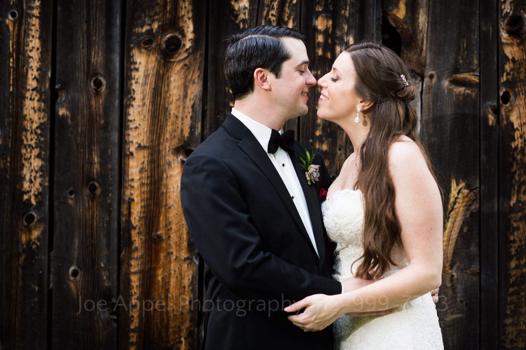 bride and groom nuzzle in front of a barn door.