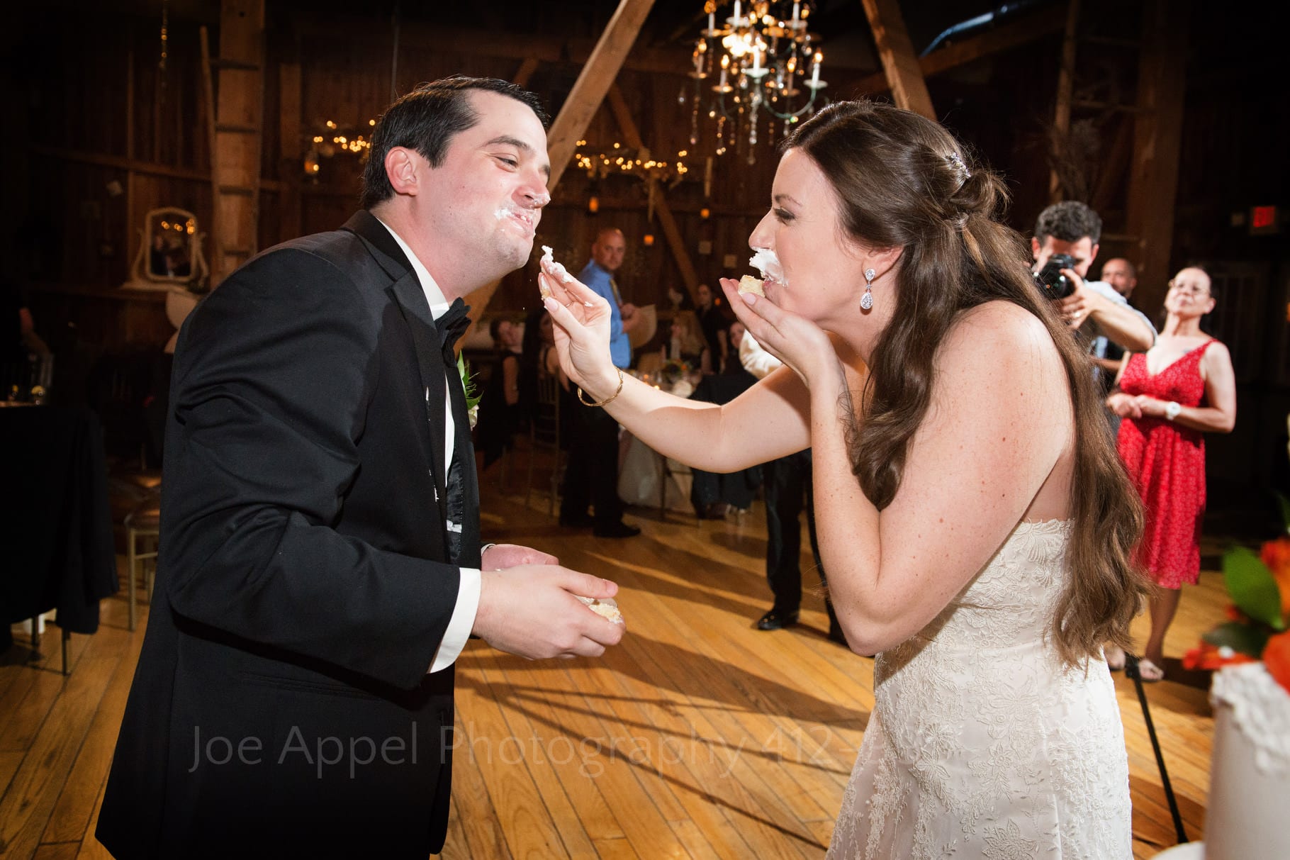 bride and groom laugh as they smear cake on each other's faces during their Chanteclaire Farm Wedding.