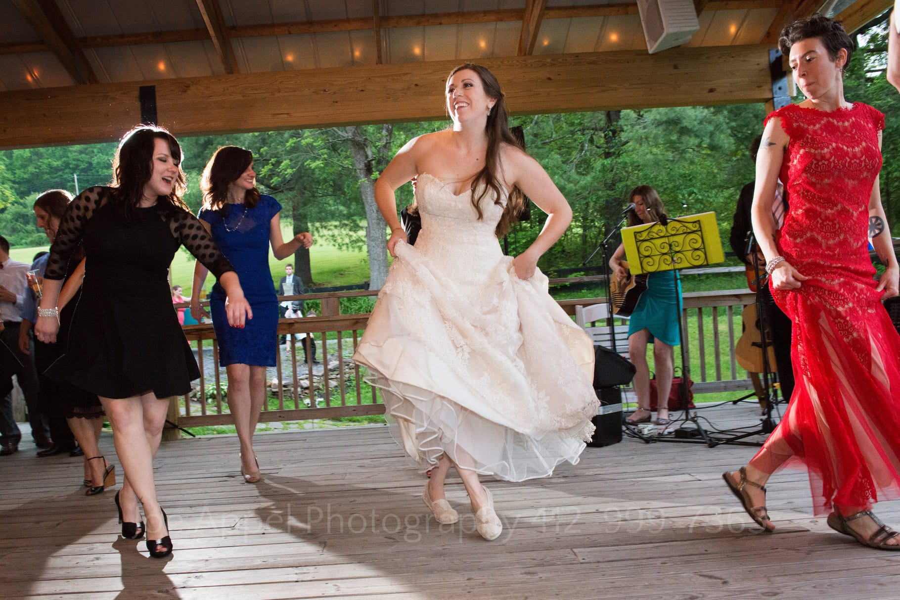 Bride dances a jig with a woman in a black dress and a woman in a red dress during their Chanteclaire Farm Wedding.