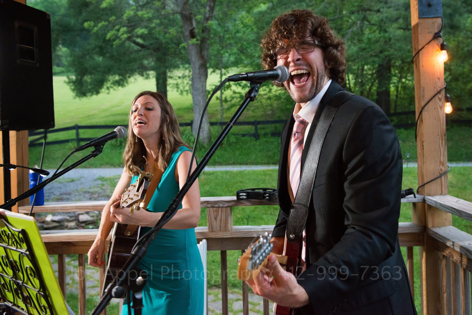guitar player sings passionately into a microphone as a woman in a blue dress accompanies him during a Chanteclaire Farm Wedding.