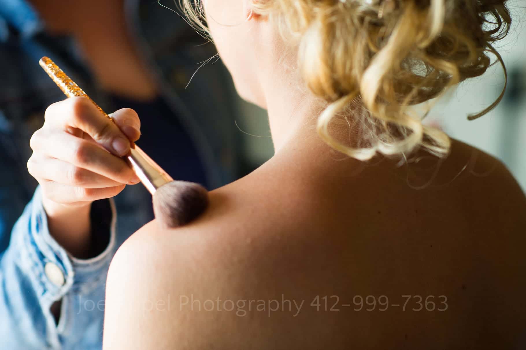 A bare shoulder gets a bit of makeup applied to it as a bride prepares for her wedding.
