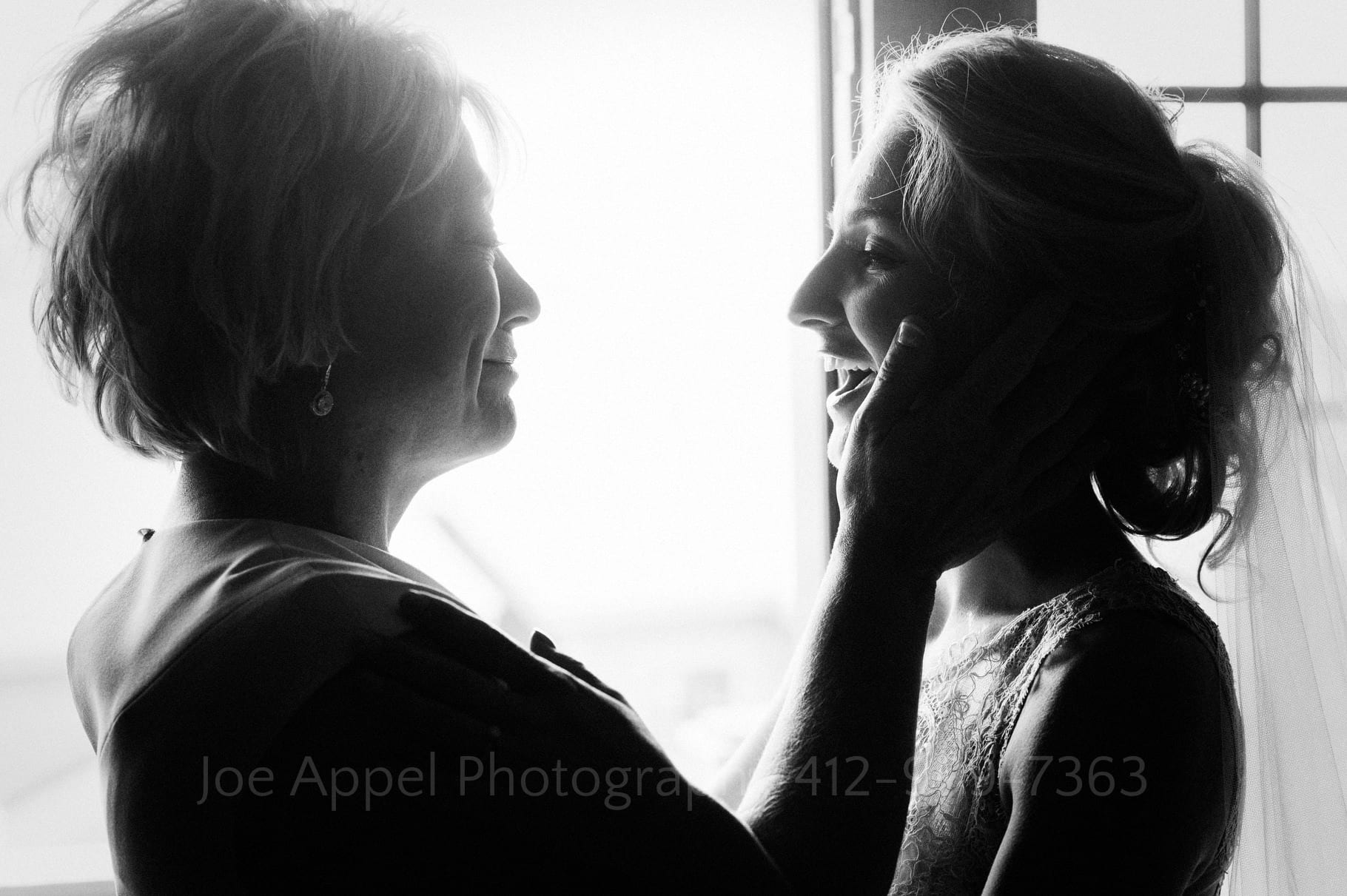 Black and white photo that is almost a silhouette of a mother caressing the cheek of her daughter on her wedding day.
