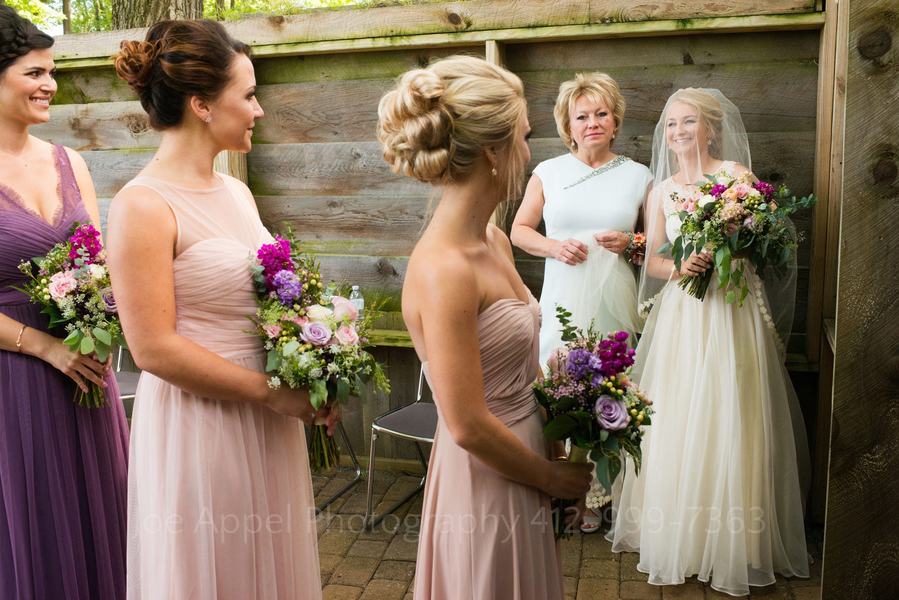A bride stands next to her mother as she watches bridesmaids line up to walk down the aisle at the beginning of her wedding ceremony.