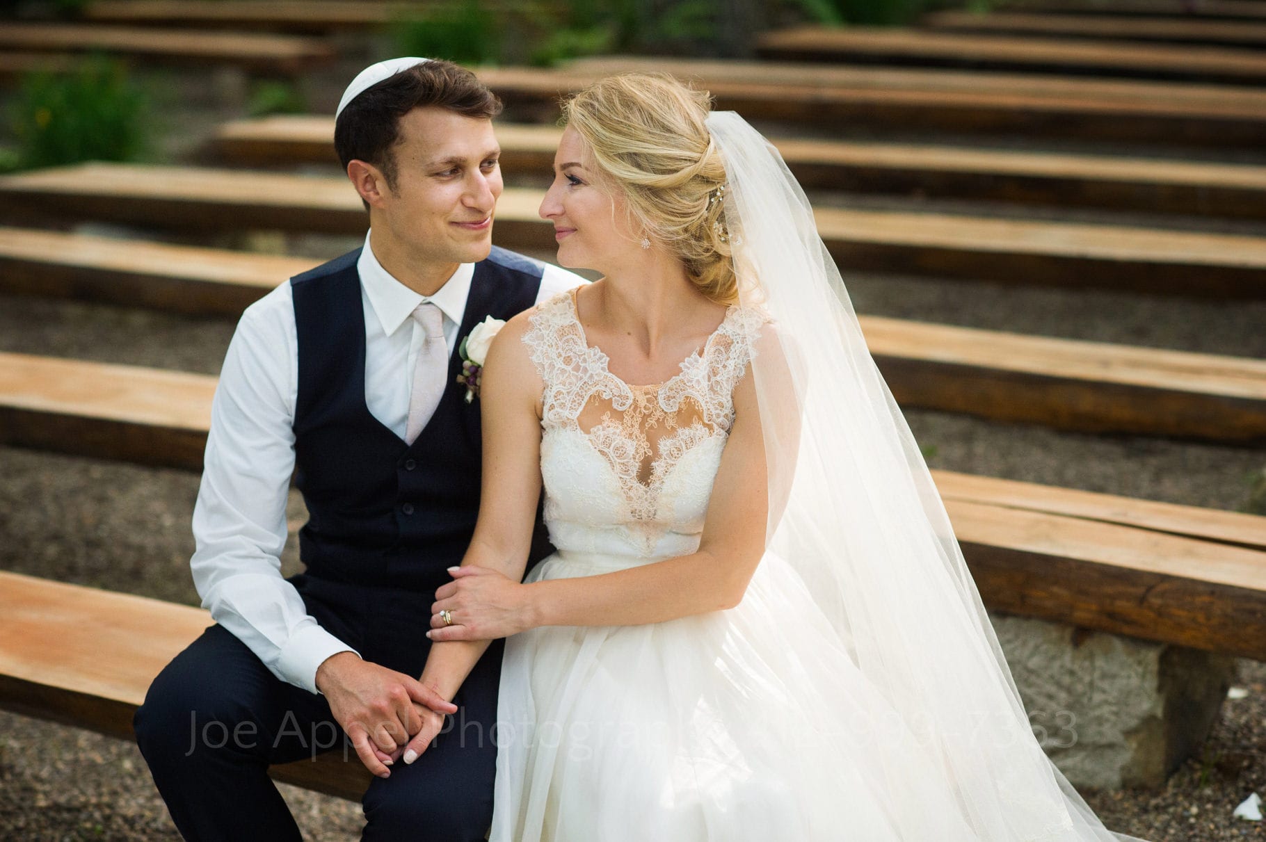 Portrait of a bride and groom smiling as they sit together on rough sawn wooden benches during their Seven Springs Wedding.