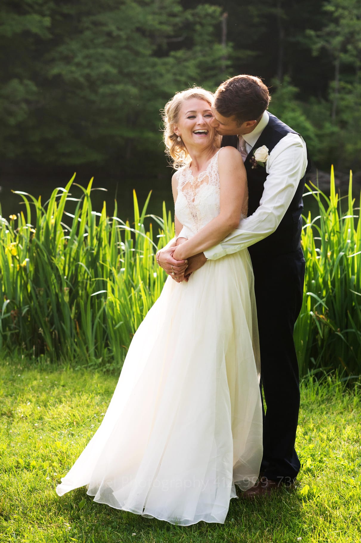 A bride leans into her groom as he embraces her from behind and kisses her neck during their Seven Springs Wedding.