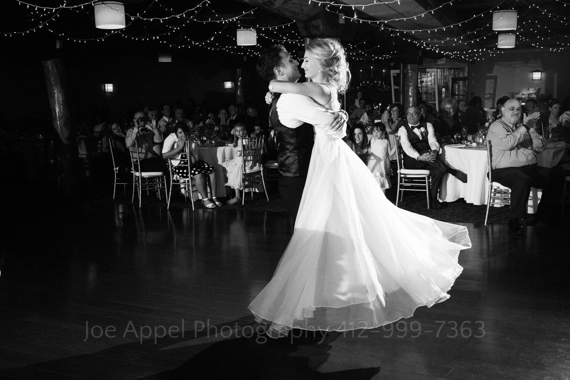 A bride's dress floats in the air as her groom picks her up and spins her around at the end of their first dance during their Seven Springs Wedding.