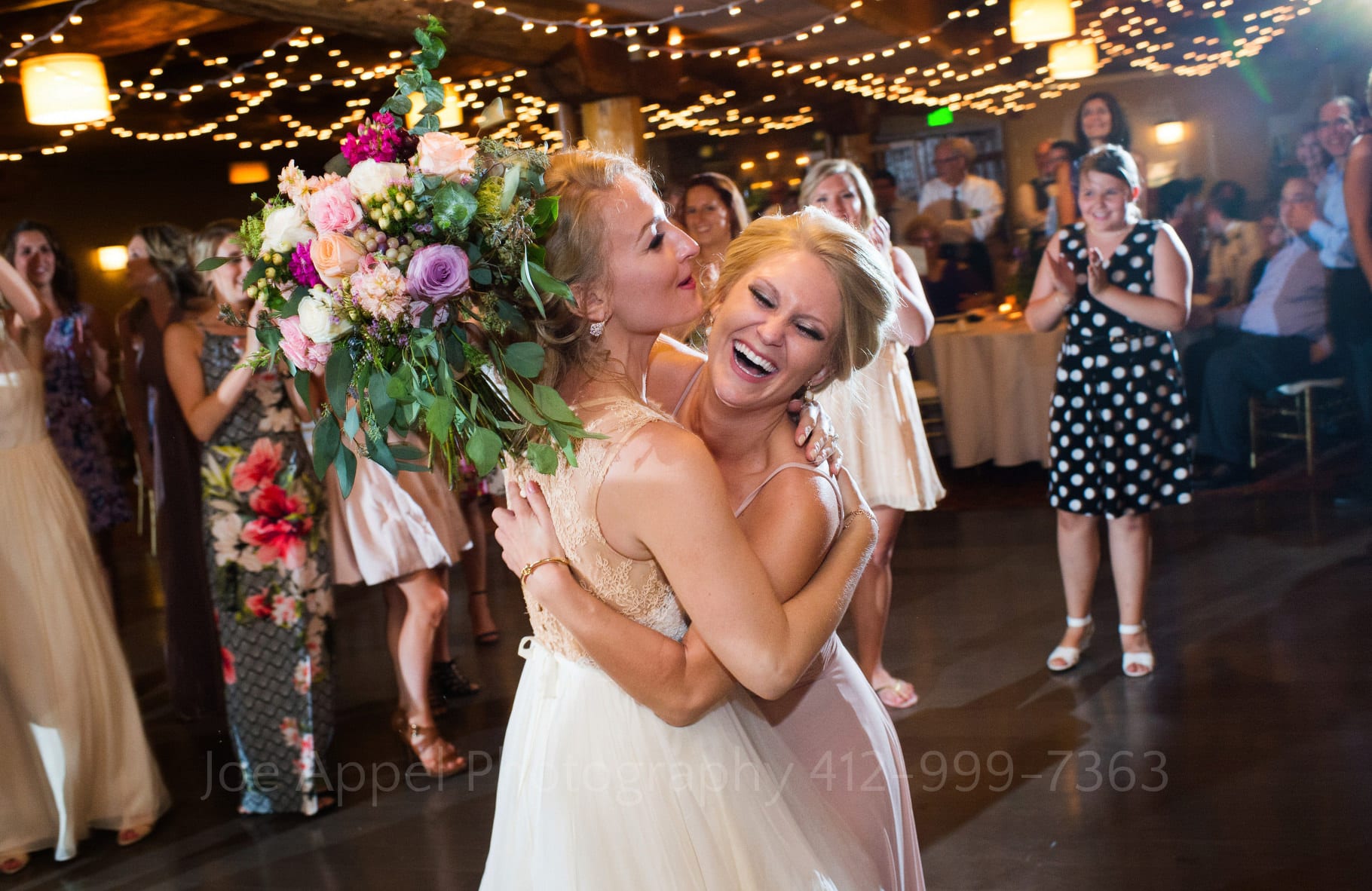 Bride is embraced by a laughing bridesmaid who holds the large bouquet that she just caught in her hand during their Seven Springs Wedding.