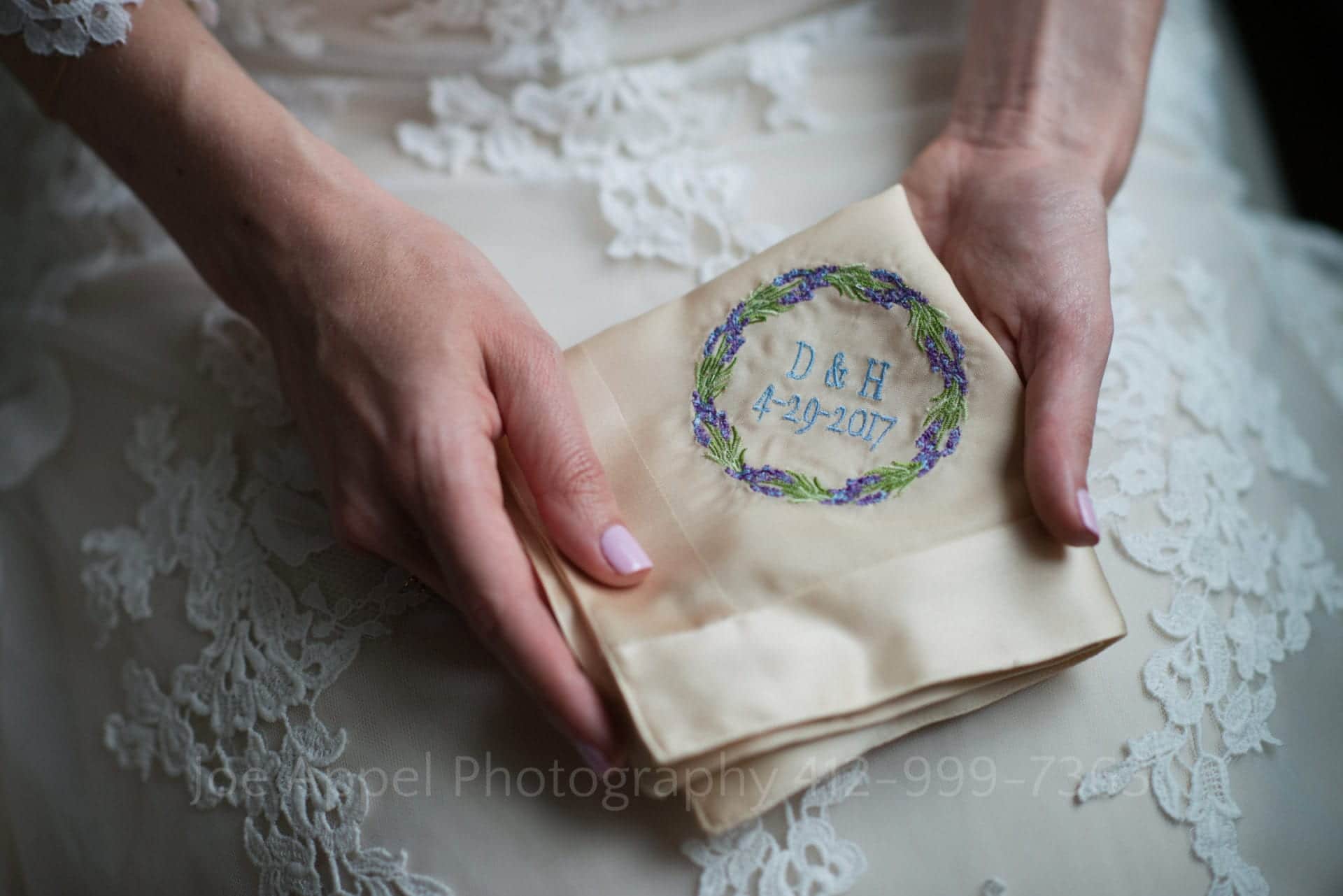 A bride holds an embroidered handkerchief with her and her husband's initials and their wedding date.