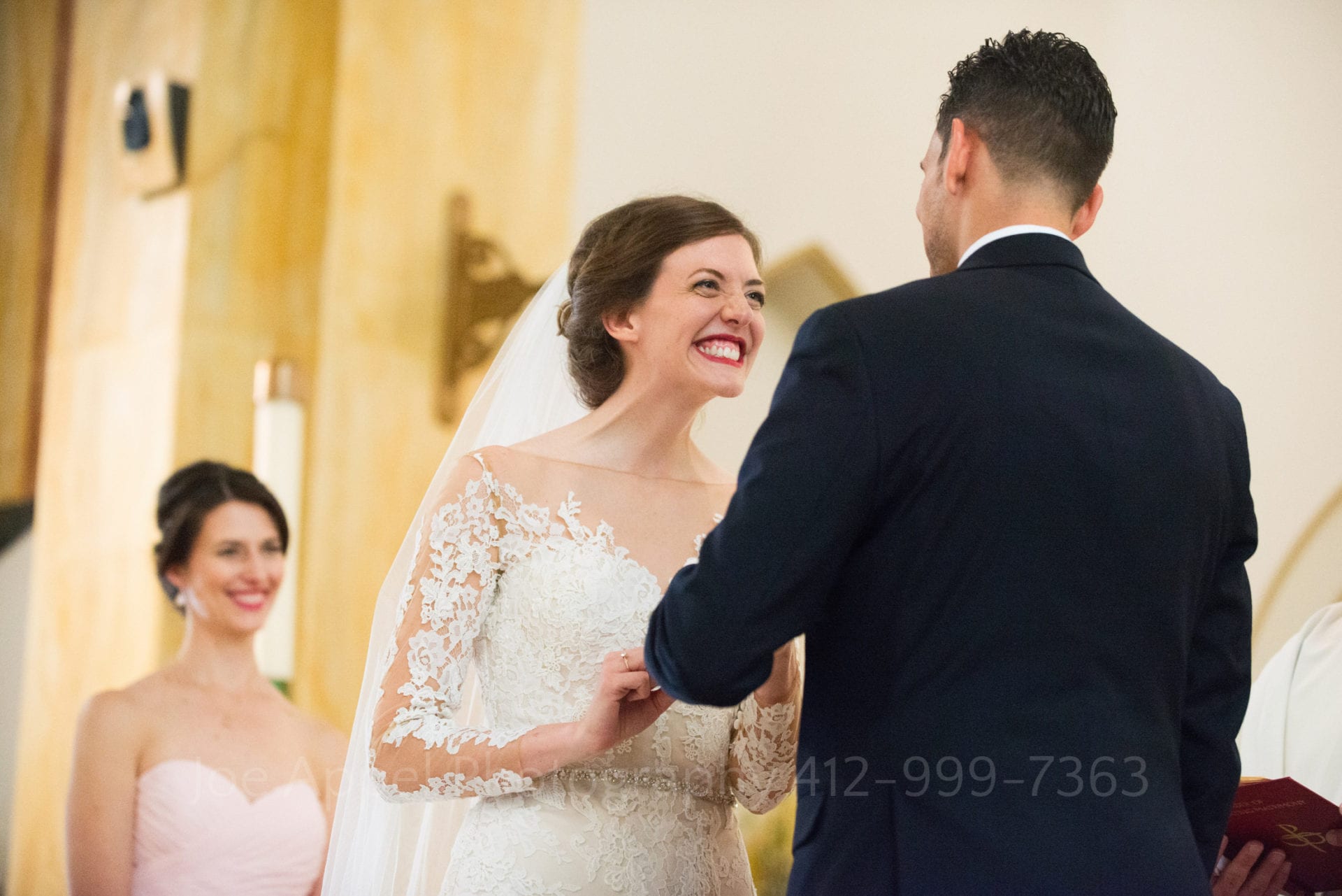 Bride looks at her groom with a huge grin as they exchange vows on the altar of a church.