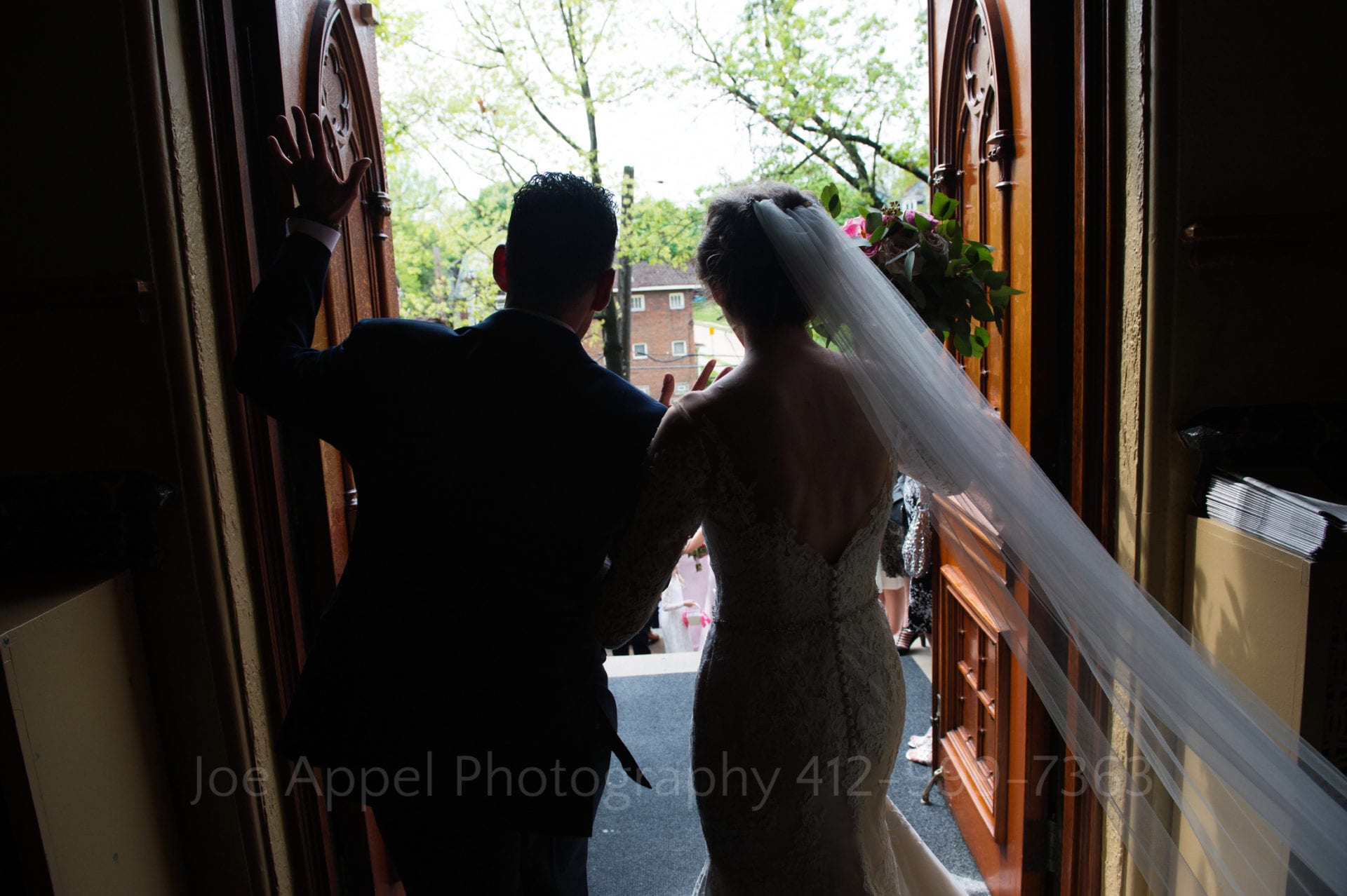 Bride and groom in silhouette as they walk out of the doors of the church after their wedding.