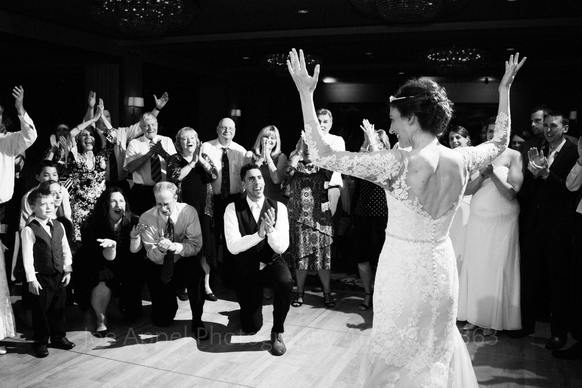 Bride holds her hands up in joy as she is surrounded and serenaded by her family and friends.