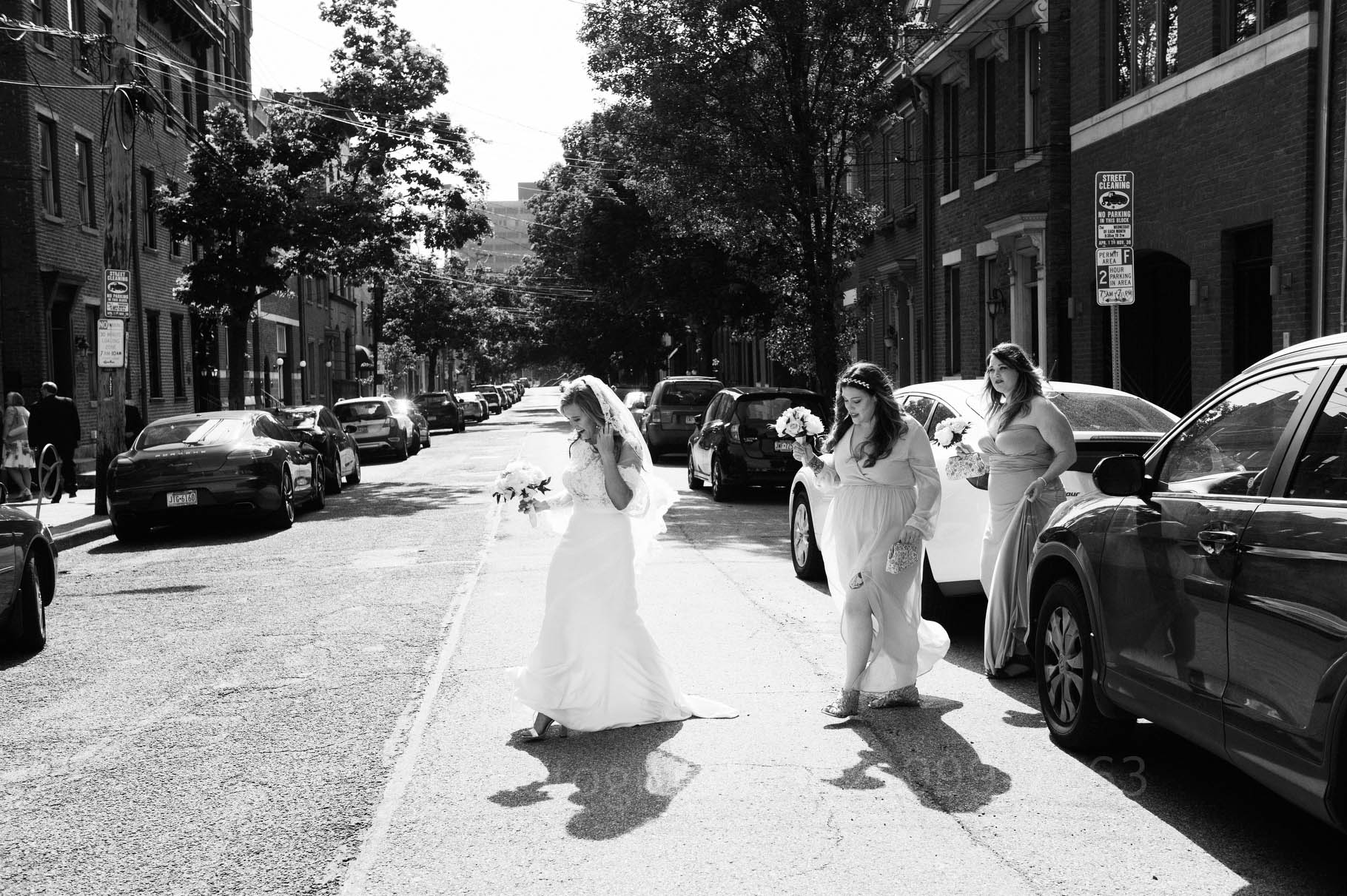 A bride steps across a city street filled with row houses as she makes her way to the wedding venue.