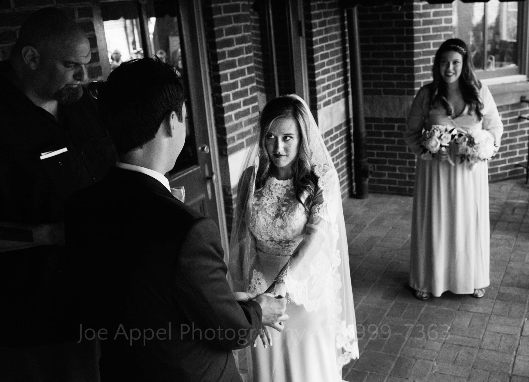 Seen from above the groom's shoulder, a bride looks up as he places a ring on her finger.