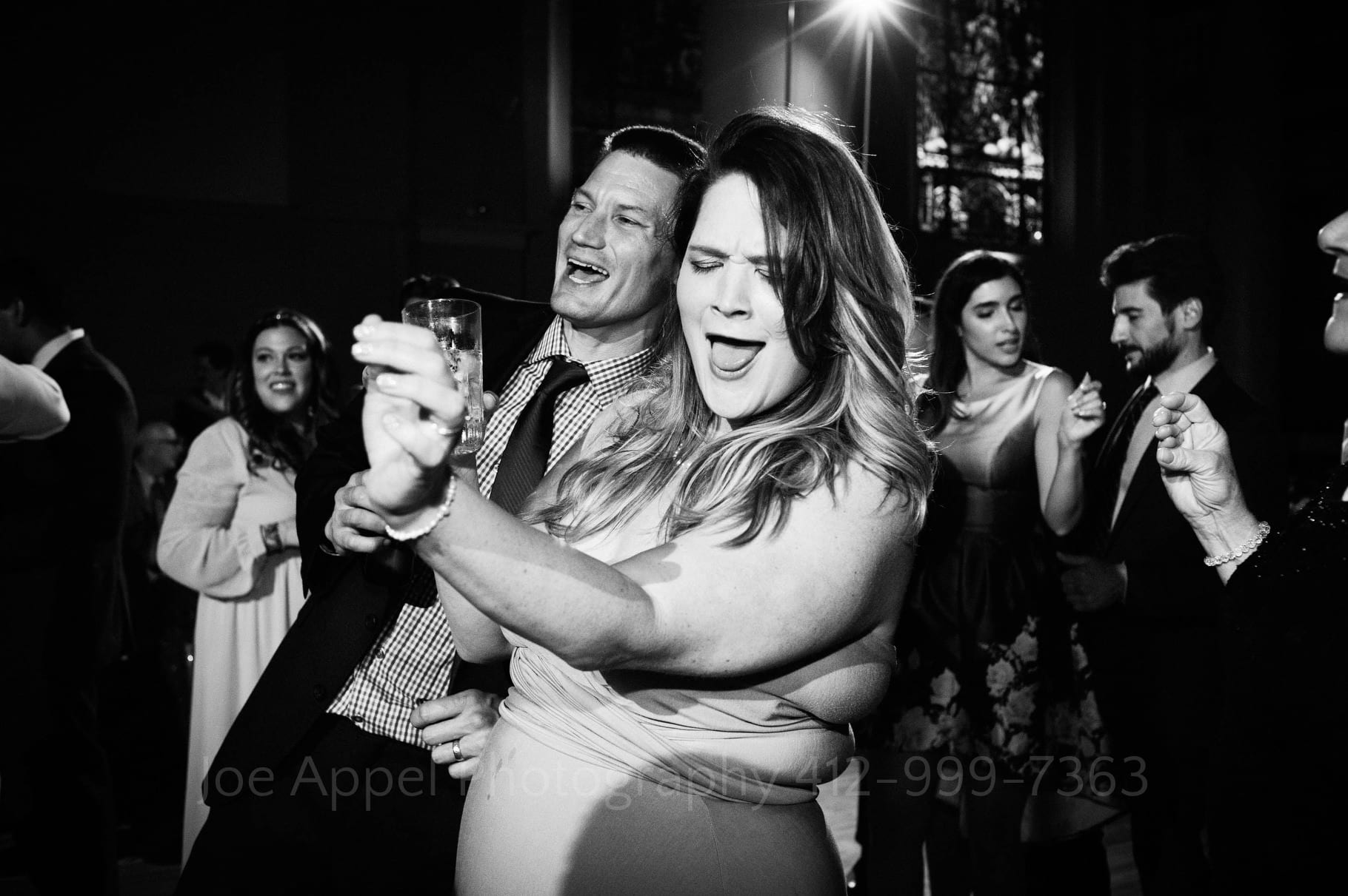 A smiling woman and man dance side by side during a wedding reception.
