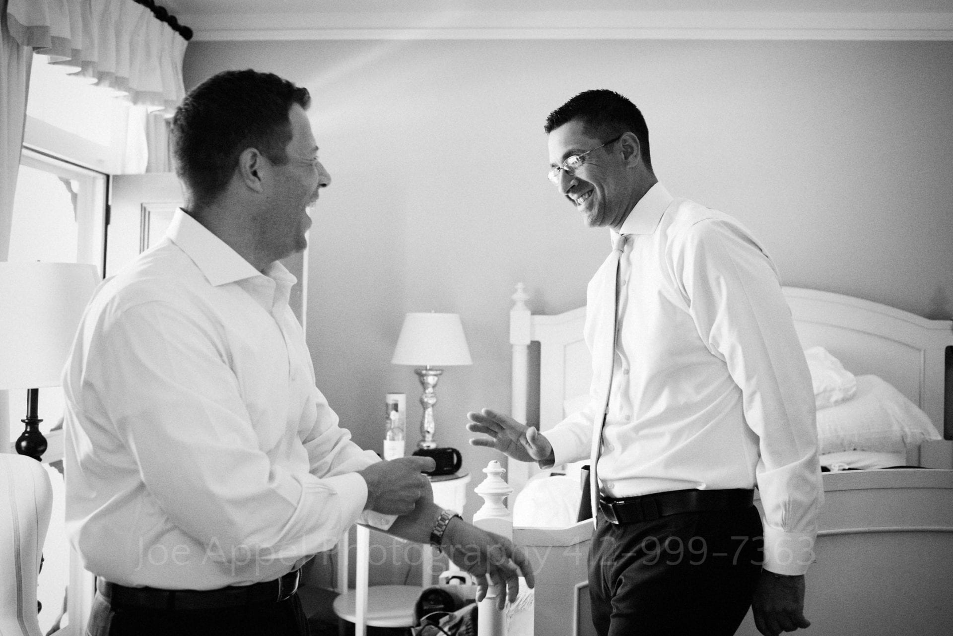 Two men laugh as they get dressed in a hotel room during their Omni Bedford Springs Resort Wedding.