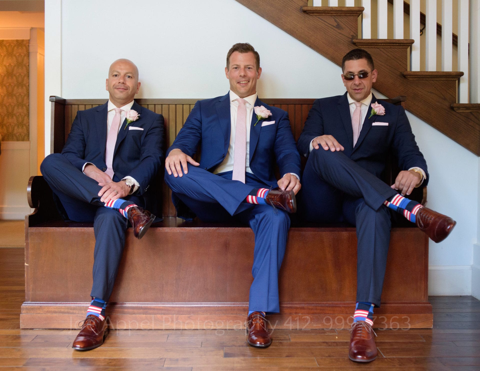 A groom and his groomsmen sit cross-legged on a bench in their blue suits and brown shoes during their Omni Bedford Springs Resort Wedding. They show off their American flag colored socks.