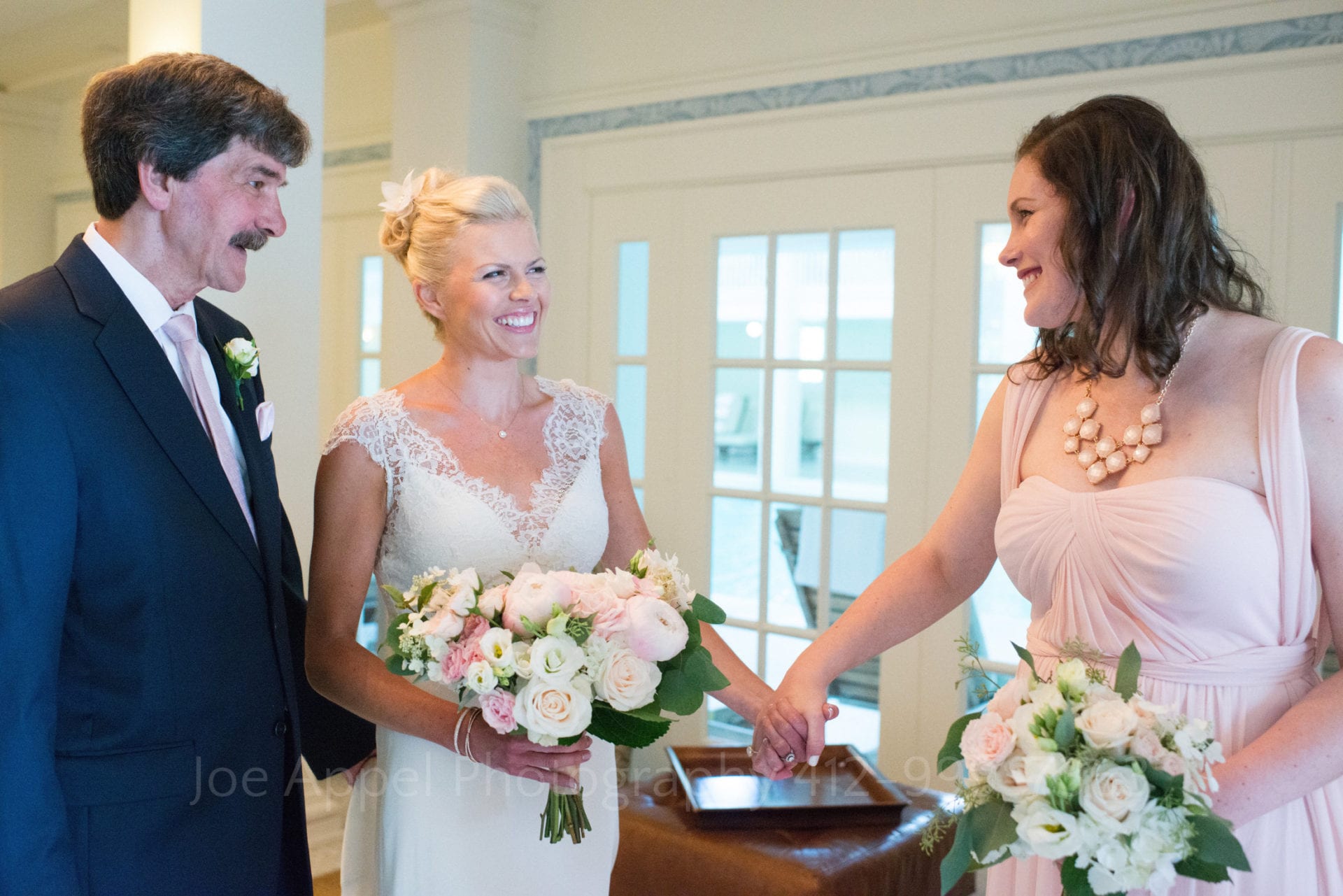 A bride holds hands with her sister as she stands between her and her father before they walk down the aisle during their Omni Bedford Springs Resort Wedding.