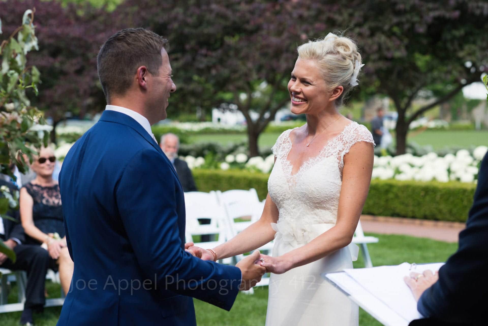 A bride smiles at her groom during their wedding ceremony while they hold both hands during their Omni Bedford Springs Resort Wedding.