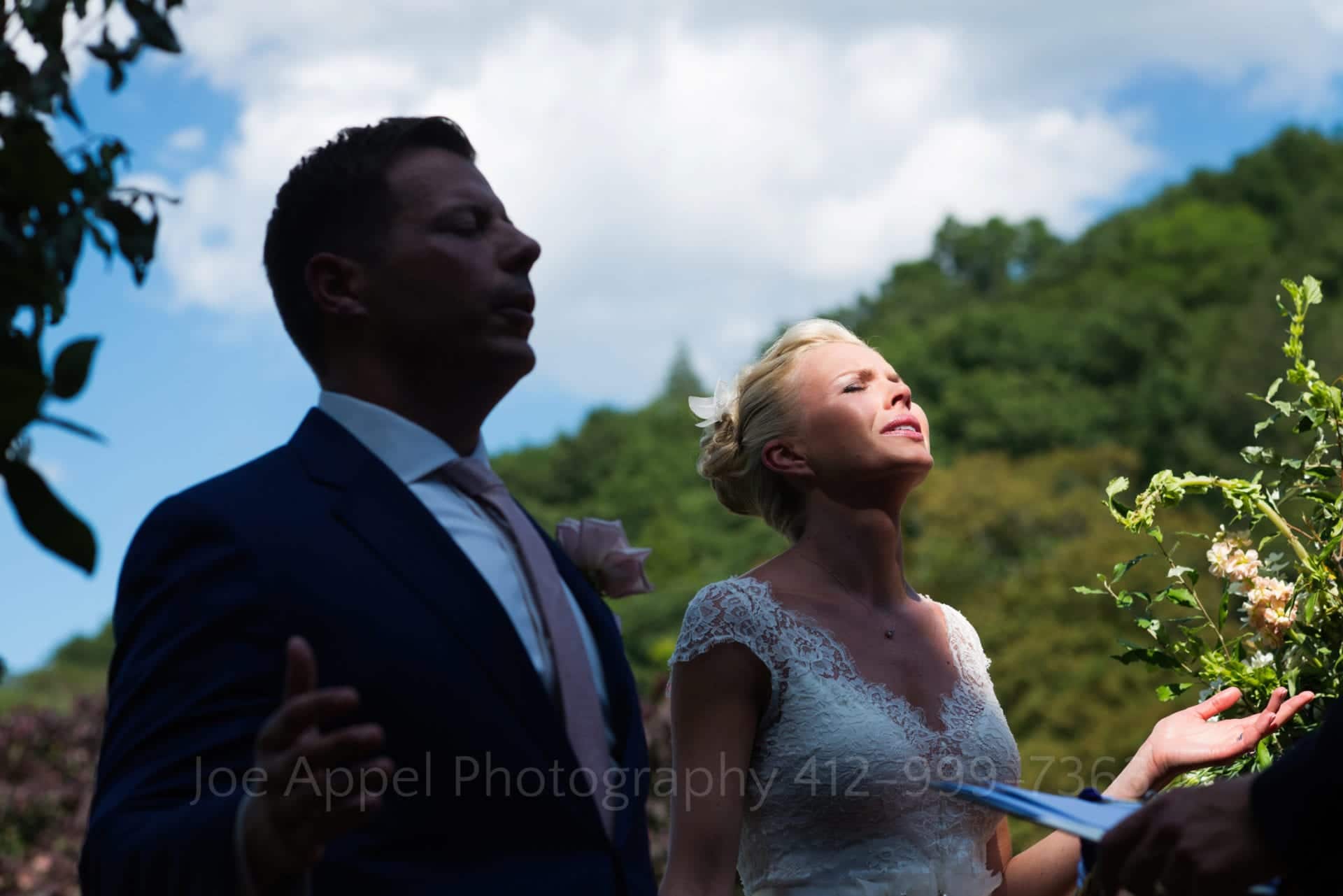 A groom stands in shadow as sunlight illuminates his bride's face while they face forward in prayer looking at the sky during their Omni Bedford Springs Resort Wedding.