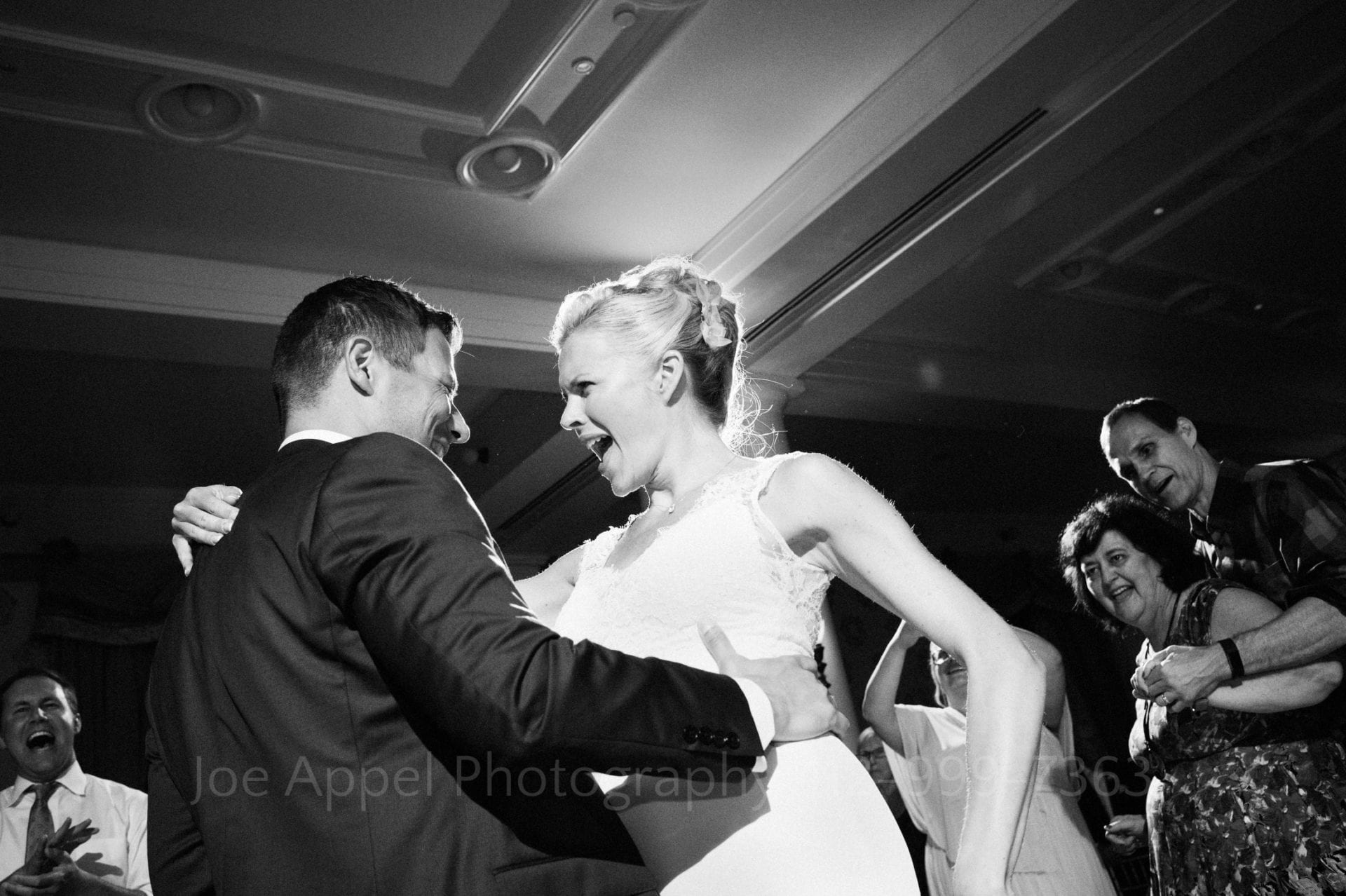 A bride yells out as she dances with her arm around the shoulder of her groom who has his hand on her waist during their Omni Bedford Springs Resort Wedding. Guests smile and laugh as they watch.
