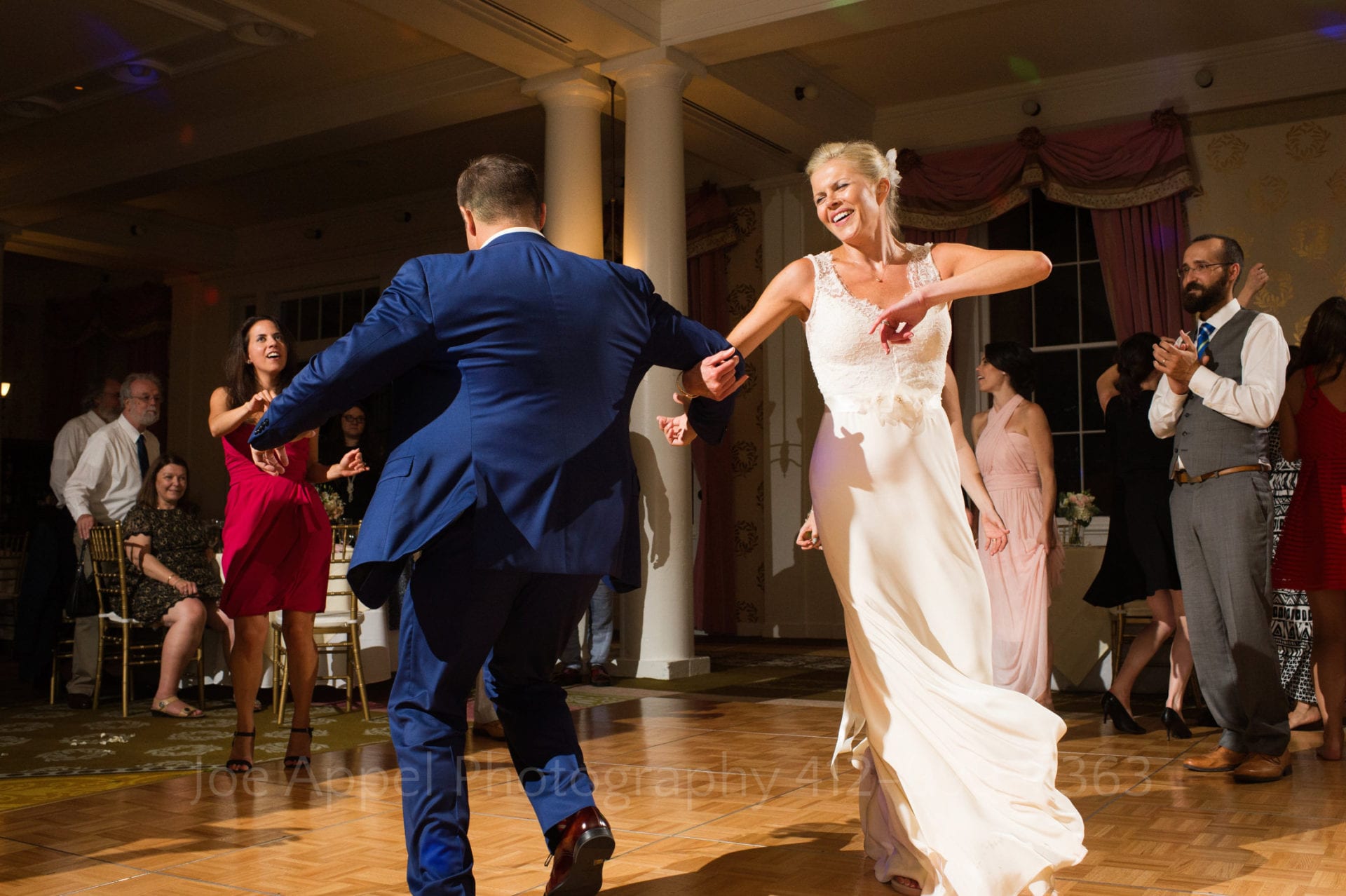 Bride and groom spin around a dance floor linked arms smiling.