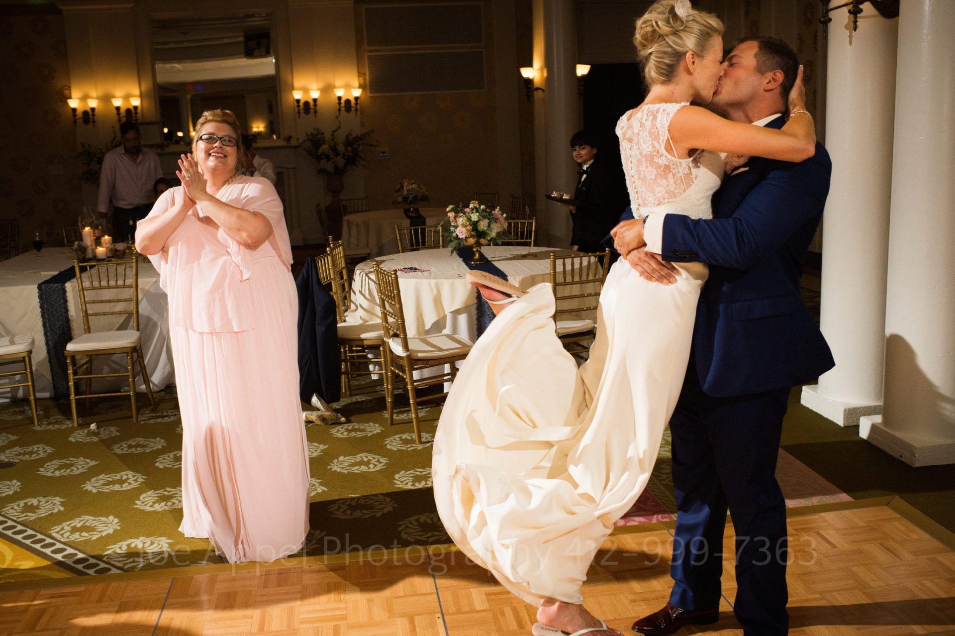 A groom lifts his bride off of the ground as he kisses her at the end of their Omni Bedford Springs Resort Wedding. A bridesmaid applauds as she looks on.