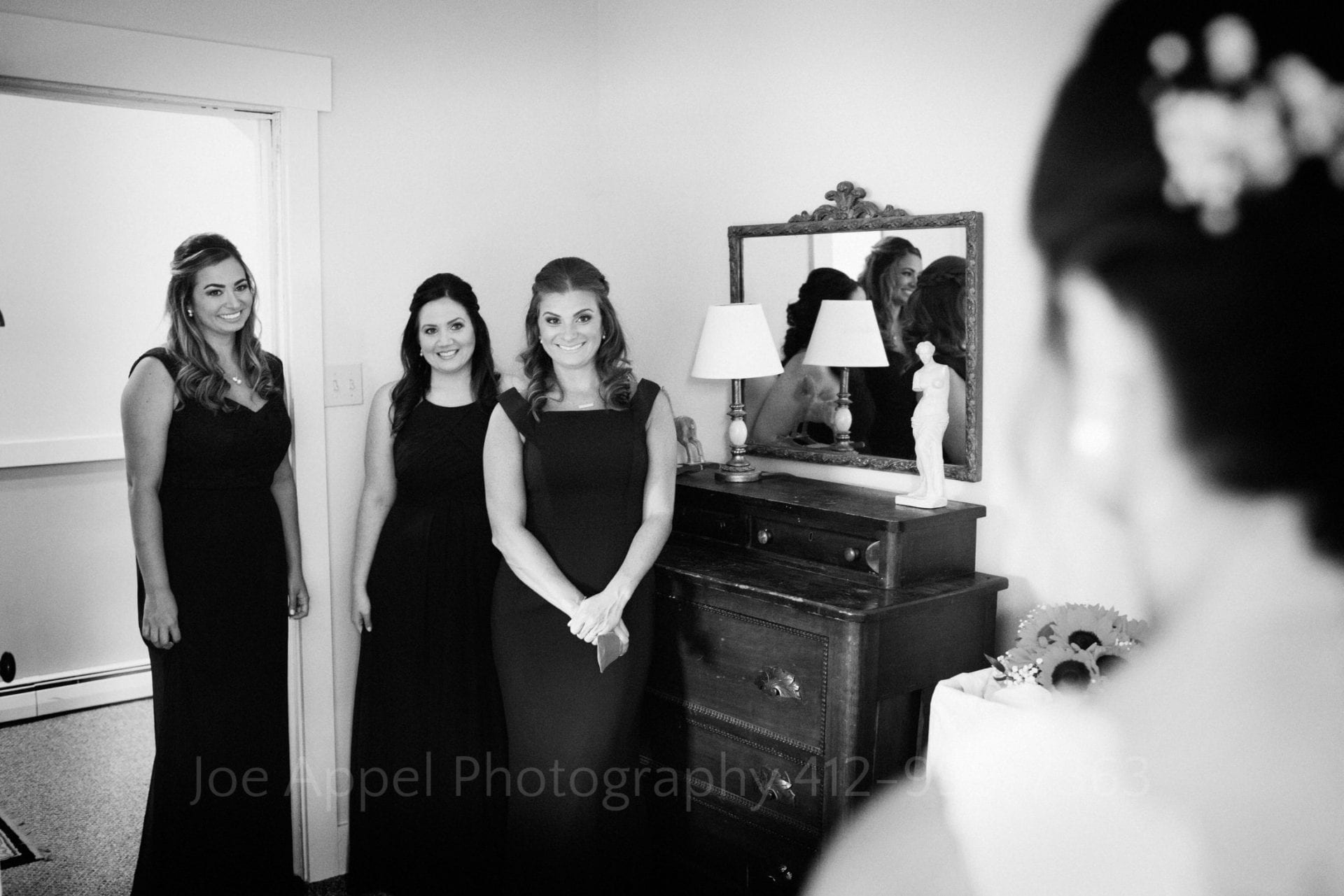 Bridesmaids look approvingly on a bride after she got her wedding dress on before her Armstrong Farms Wedding. The photo is shot over the bride's shoulder.