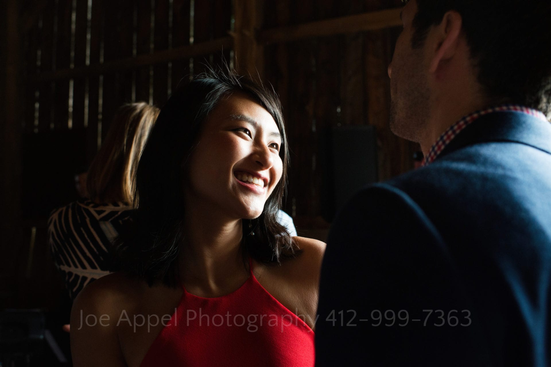 A beautiful asian woman smiles as she dances with her date. The sunlight illuminates her face in a pleasing way.