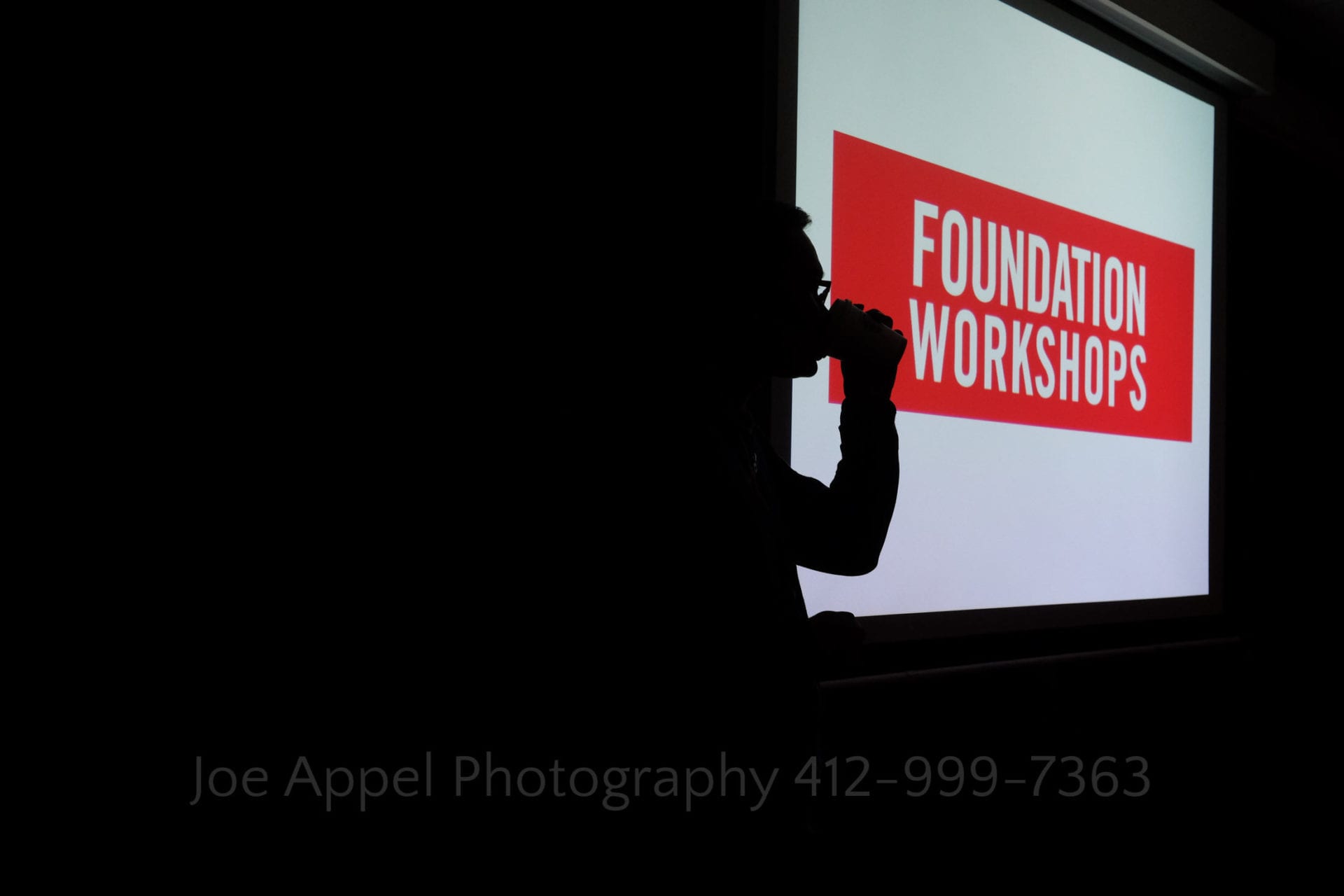 silhouette of a man drinking a cup of coffee with a screen displaying the name Foundation Workshops
