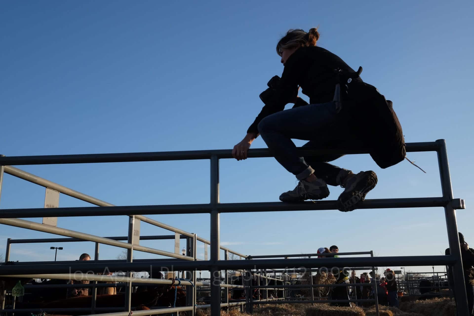 a silhouette of a photographer sitting on a corral fence