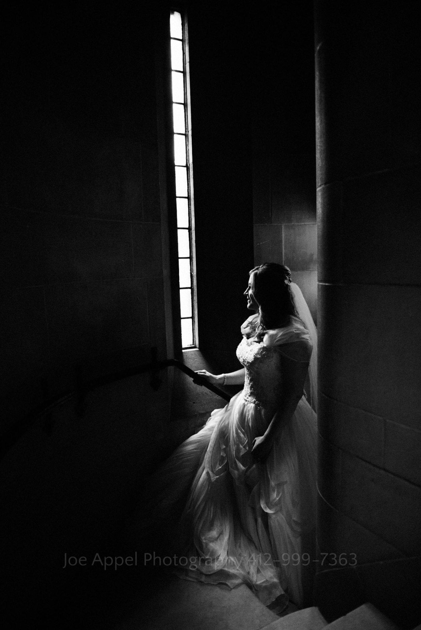 A bride is illuminated by a tall, narrow window as she walks up the stone stairs from the basement at Heinz Memorial chapel.