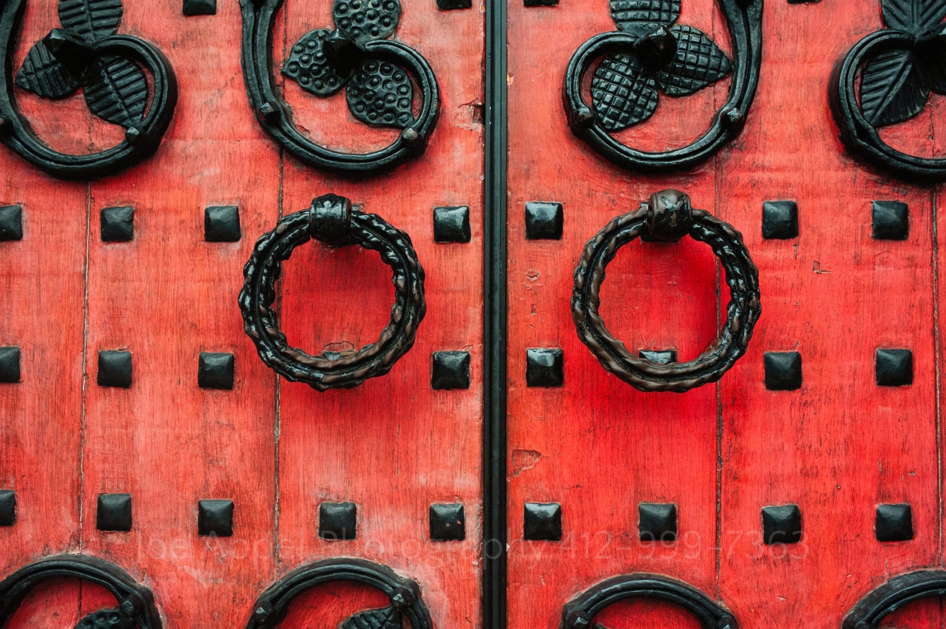 detail photo of the red-painted heavy wooden doors at Heinz Chapel. There are black rivets and fancy ironwork pulls on the door.