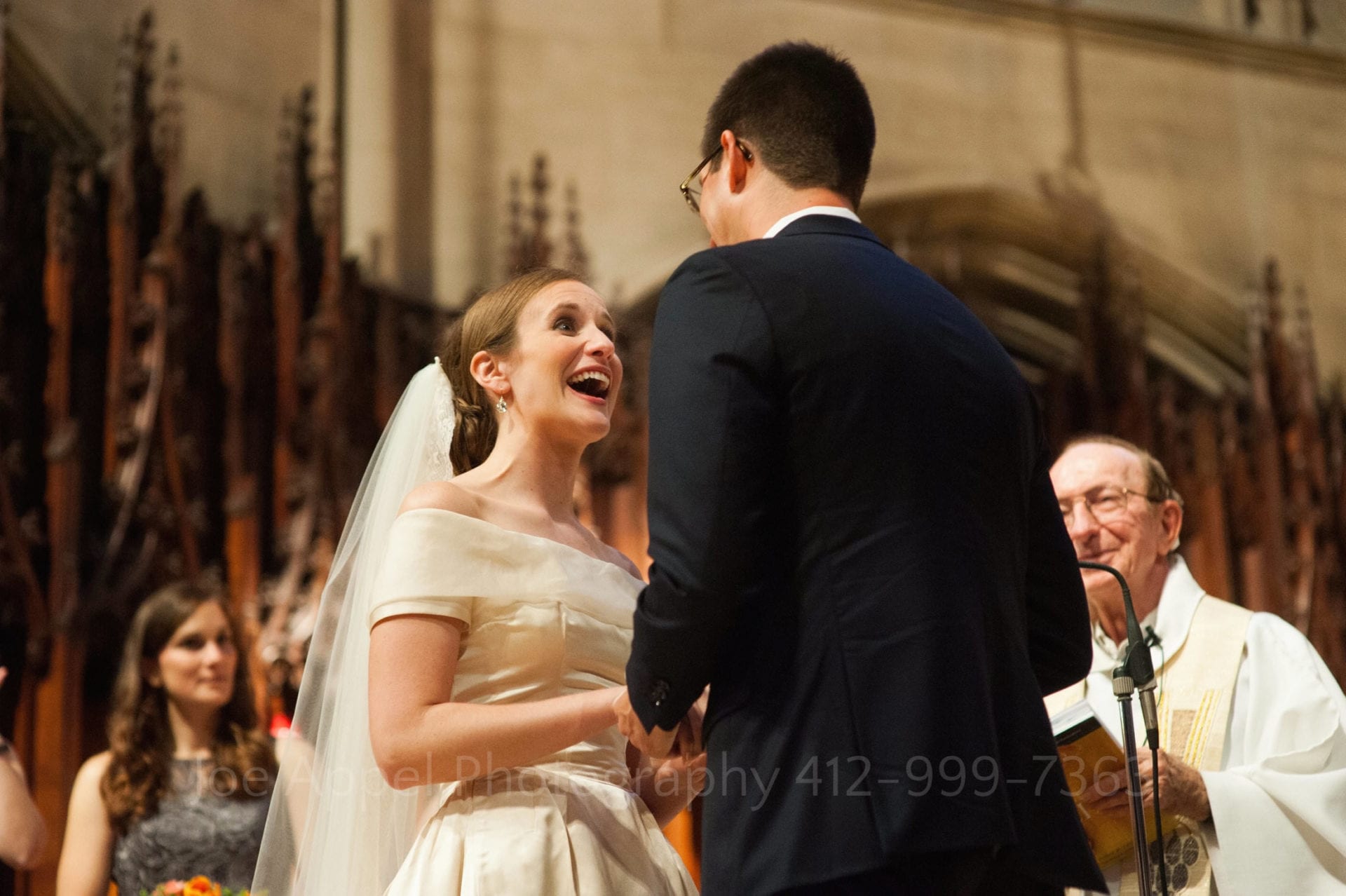 a bride smiles as she looks up at her groom as they face each other on an altar.