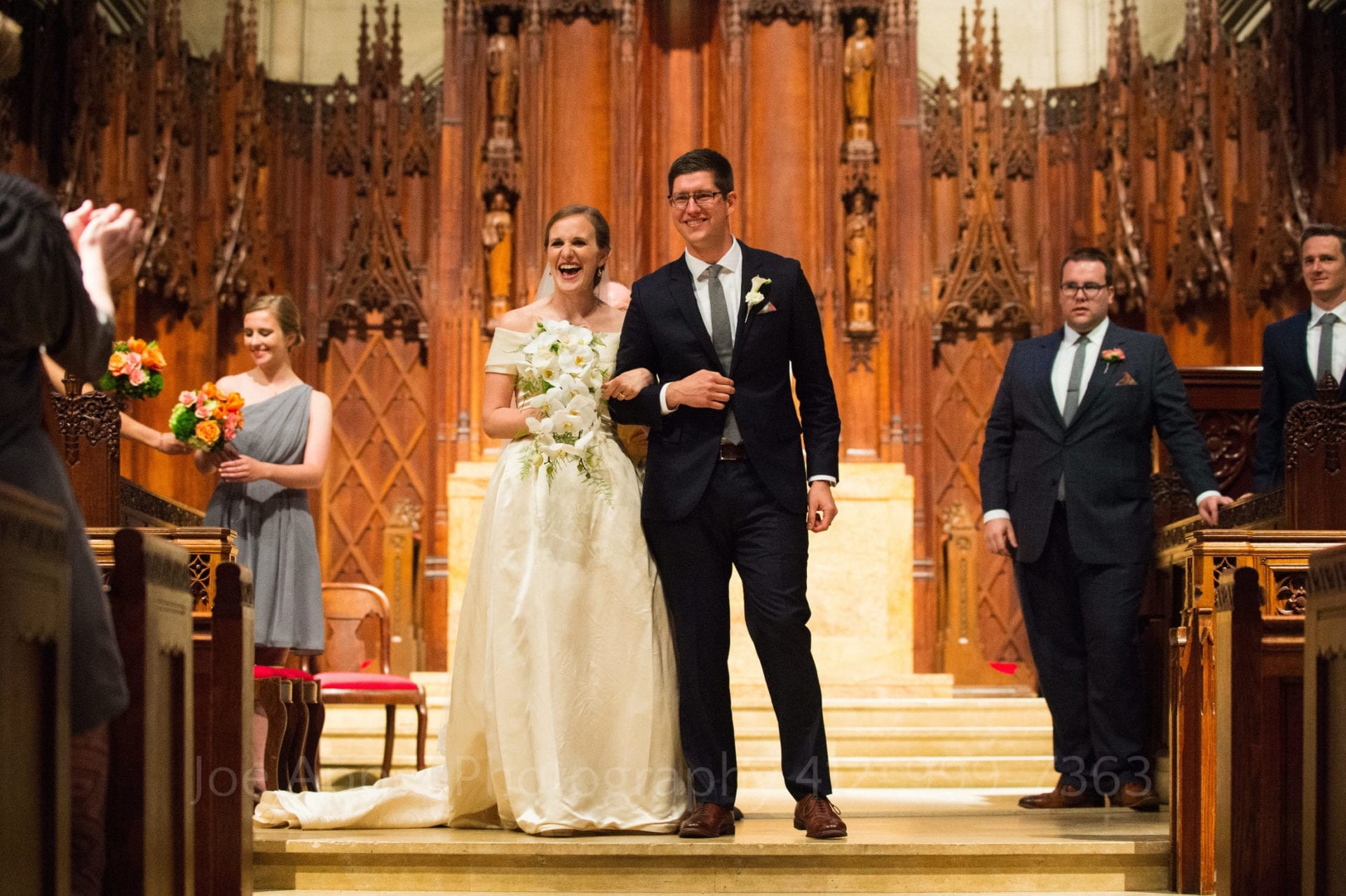 Bride and groom are presented to the audience at the end of a Heinz Chapel weddings. They're smiling broadly. 
