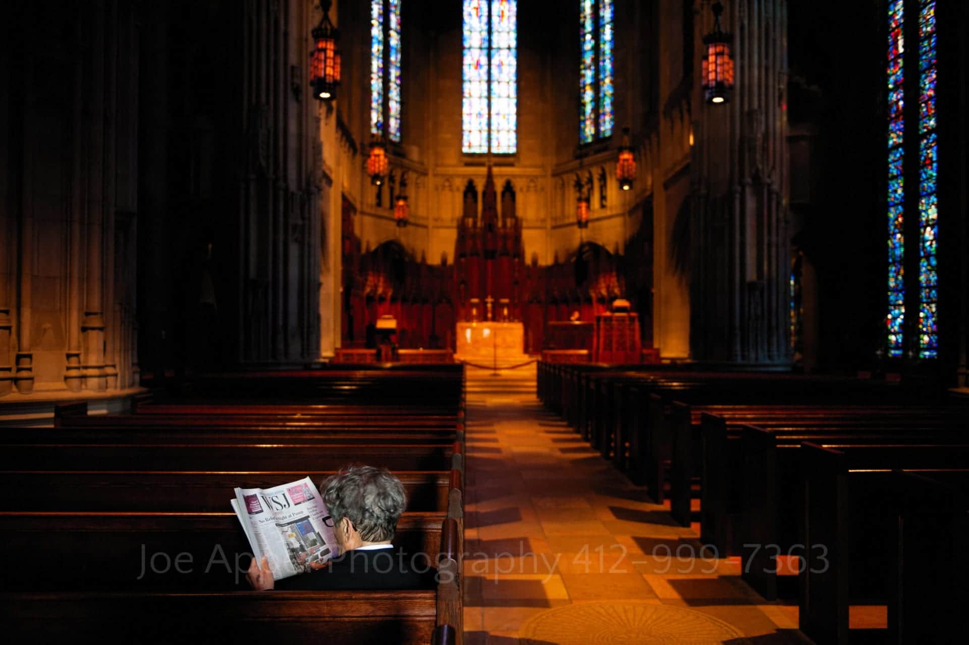 golden light illuminates the altar and interior of heinz memorial chapel as an older man sits in the sunlight in the last pew reading the wall street journal