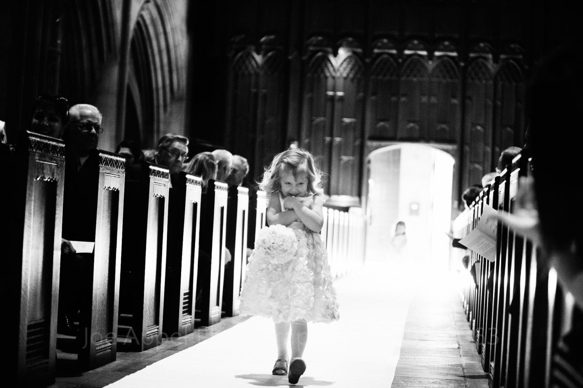 A little girl shyly walks down the aisle at heinz chapel during a wedding.