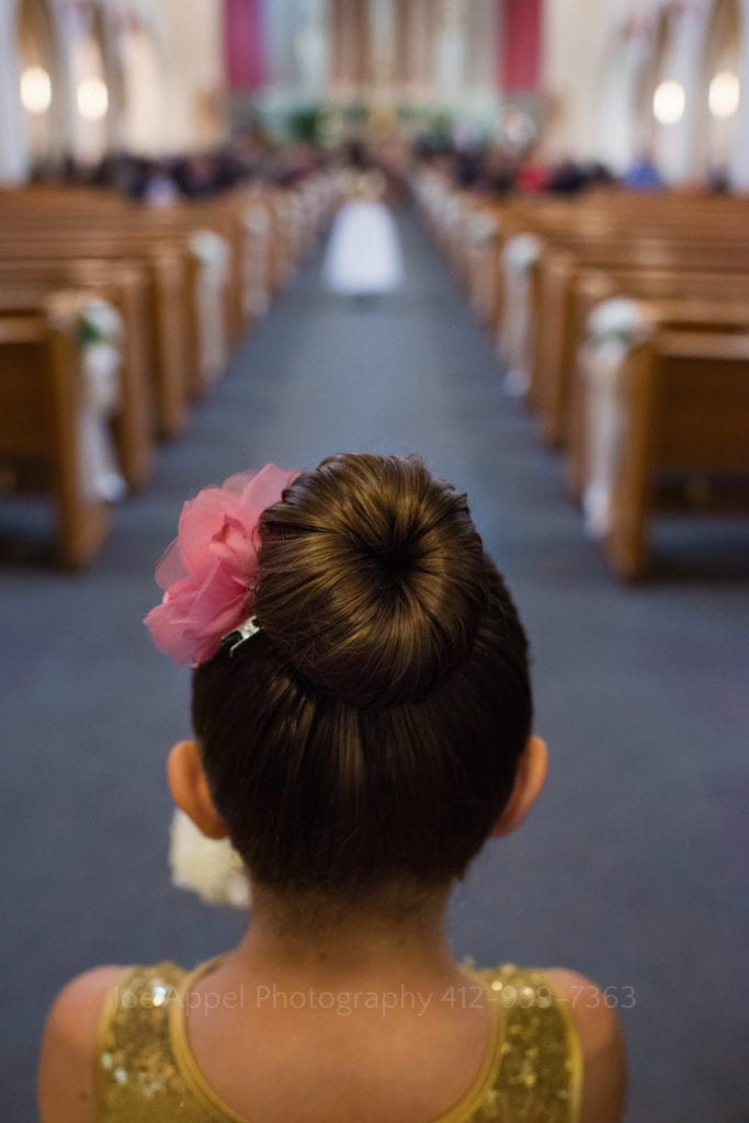 detail of the bun in the hair of a flower girl as she faces away from the camera preparing to head down the aisle at a church wedding