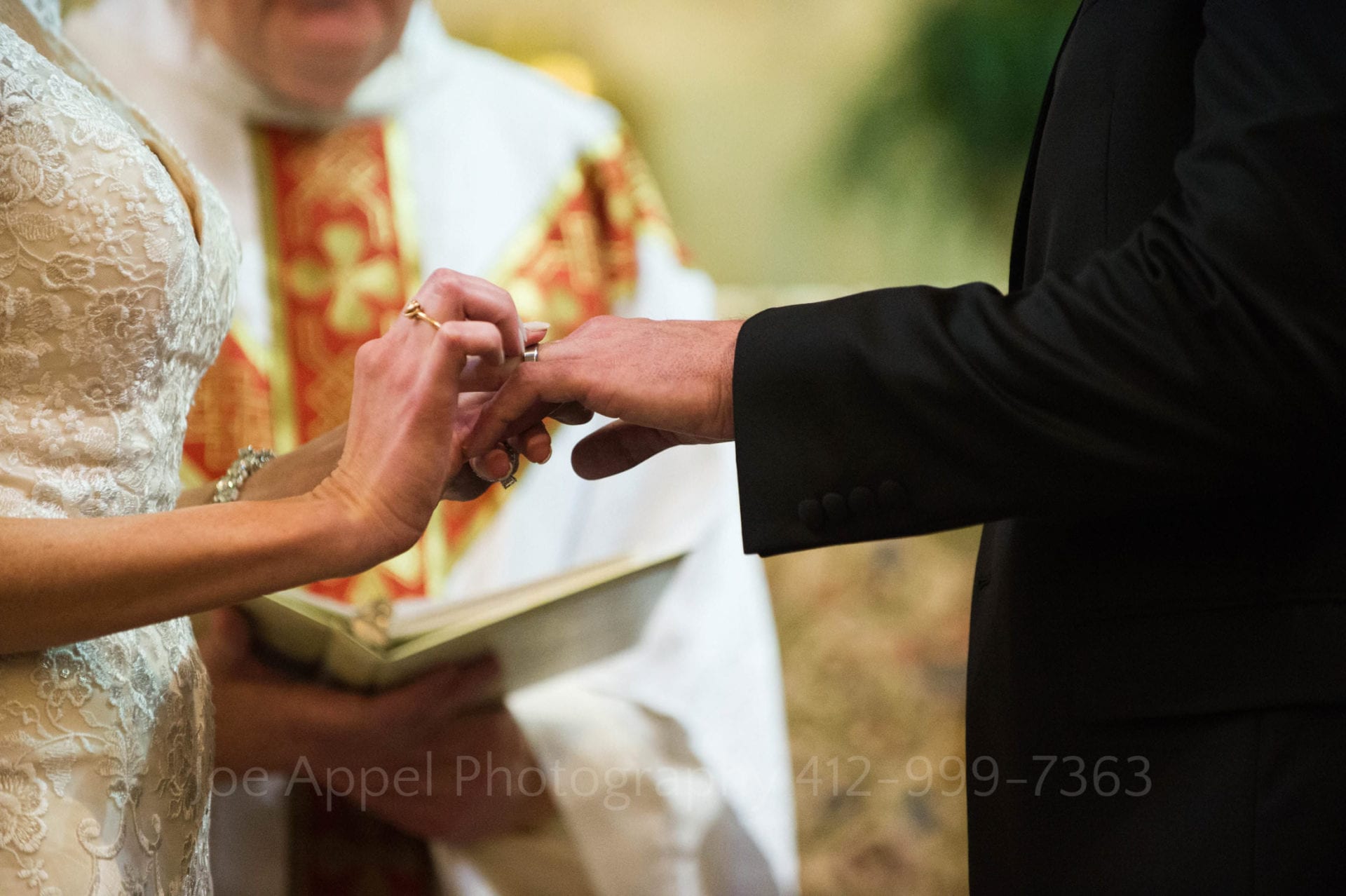 detail of a bride's hands placing a wedding band on her husband's finger.